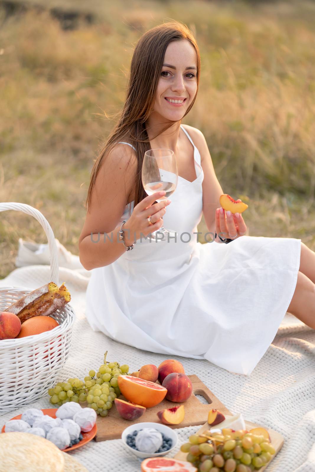 Gorgeous young brunette girl in a white sundress enjoying a picnic in a picturesque place. Romantic picnic.