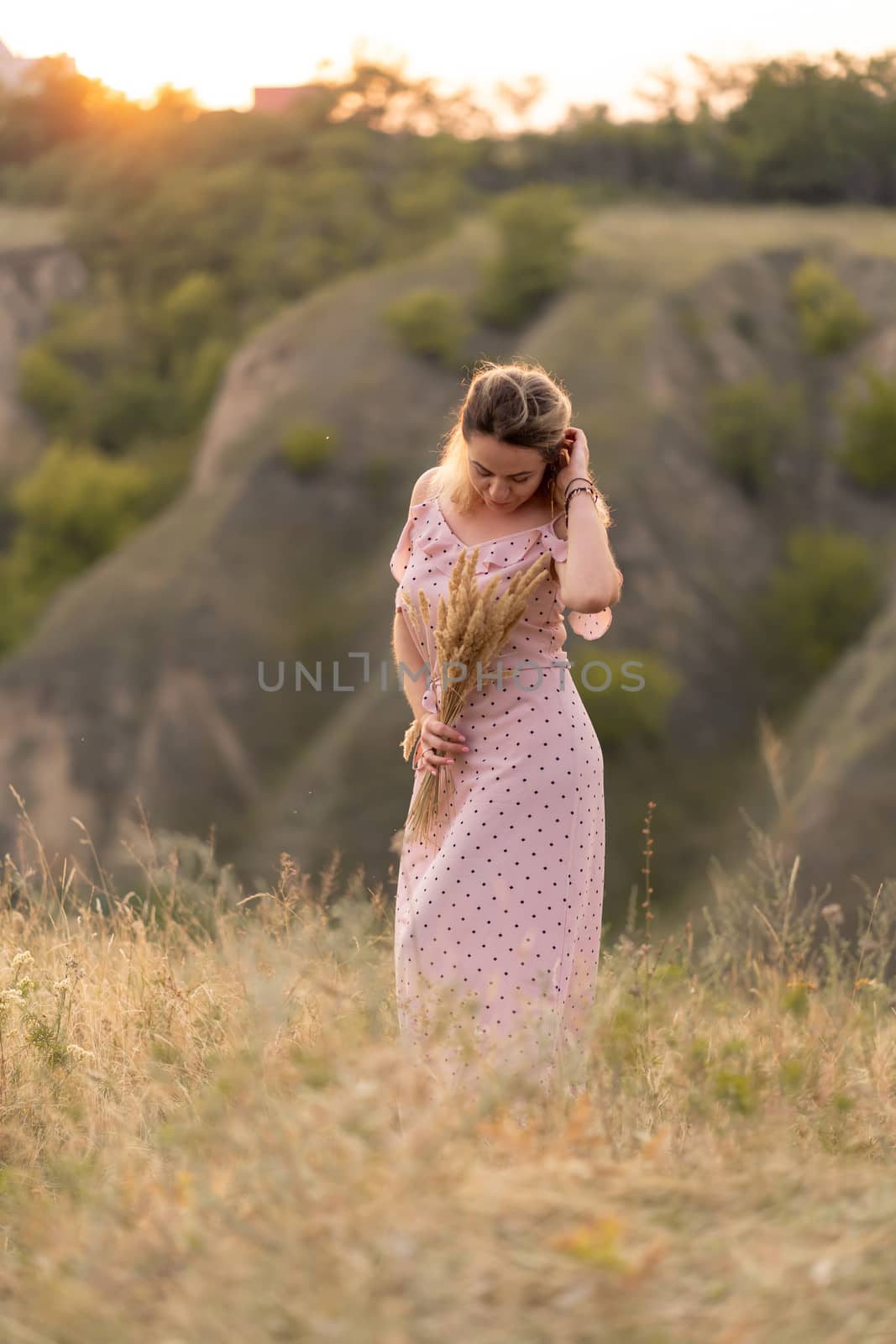 Beautiful tender girl in a white sundress walks at sunset in a field with a spikelet bouquet