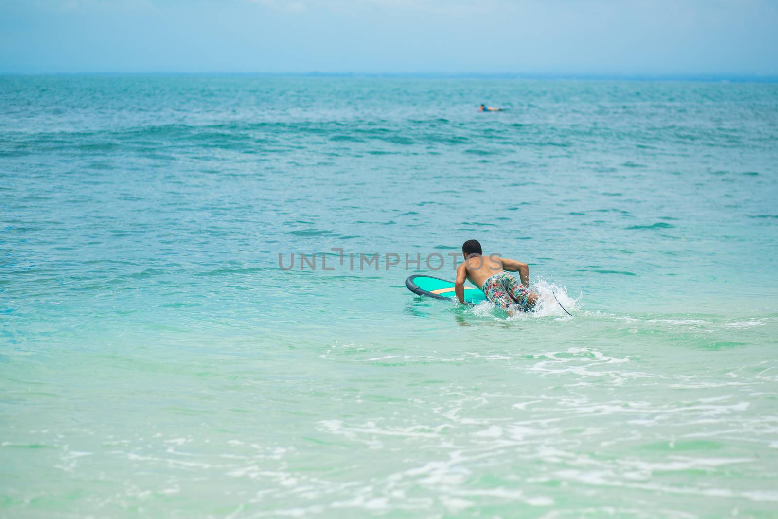 The guy is swimming on the surf board on the ocean. Healthy active lifestyle in summer vocation