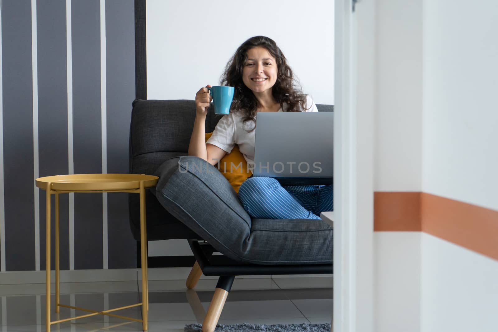 Beautiful girl sitting with a laptop on a sofa in a stylish room. Work from home. Work atmosphere in a good mood.