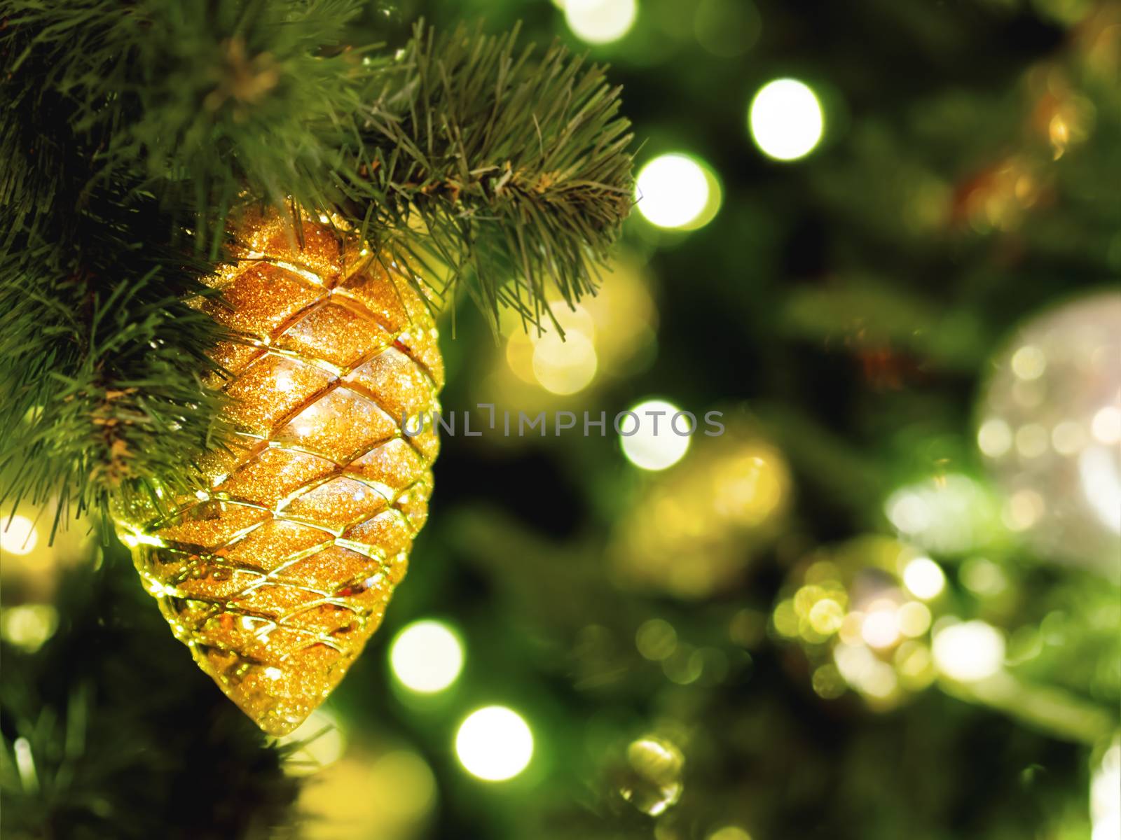 Decorative golden pine cone on Christmas tree. Festive background with light bulbs. New Year celebration.