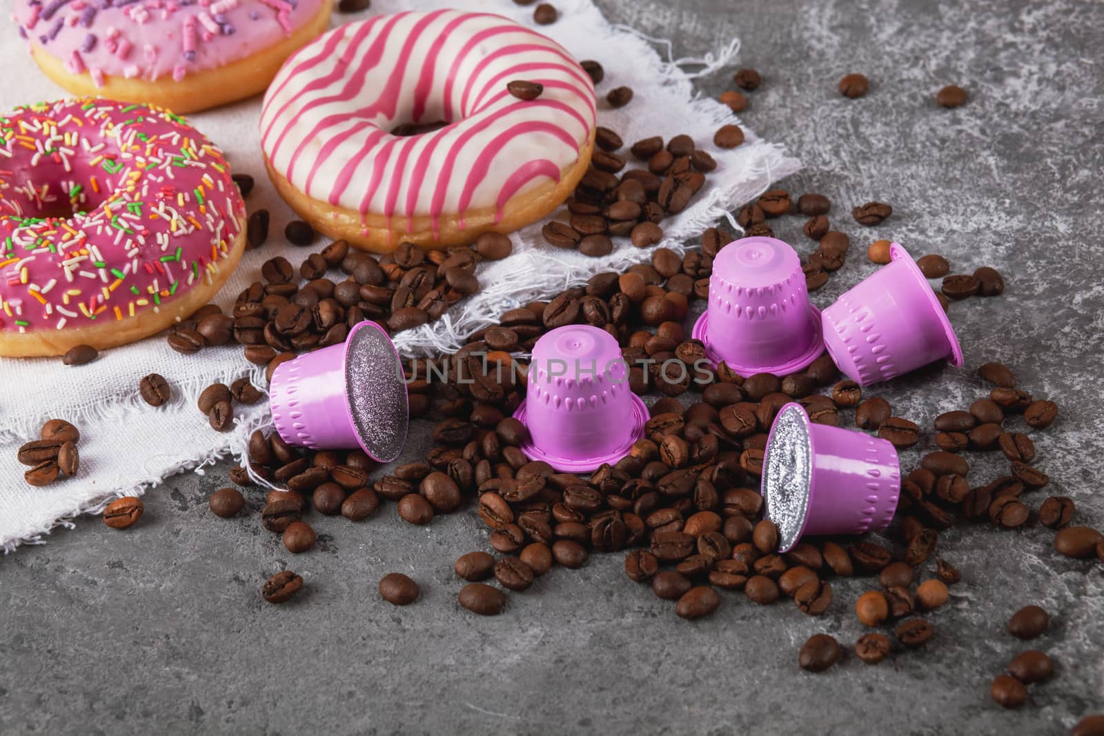 Espresso pink plastic capsules with foil and coffee beans and sweet donuts on gray concrete background