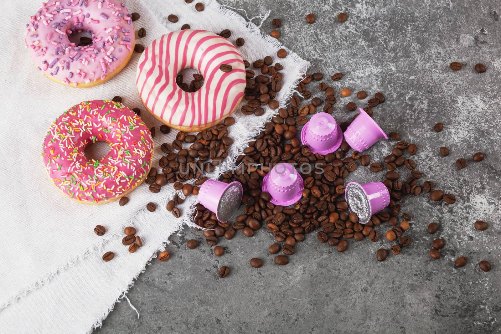 Espresso pink plastic capsules with foil and coffee beans and sweet donuts on gray concrete background