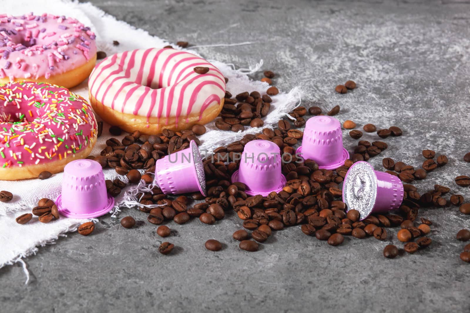 Espresso pink plastic capsules with foil and coffee beans and sweet donuts on gray concrete background