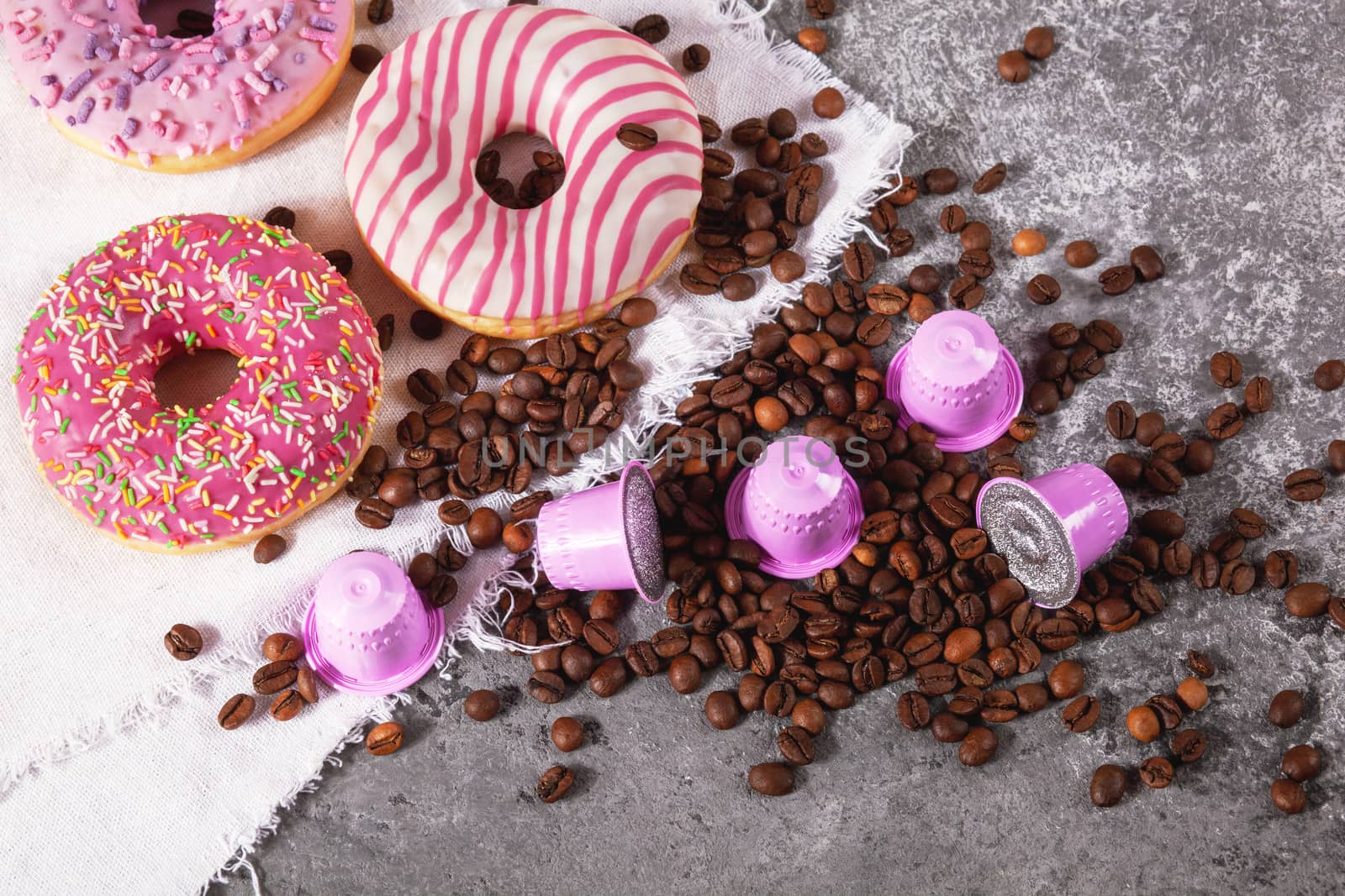 Espresso pink plastic capsules with foil and coffee beans and sweet donuts on gray concrete background