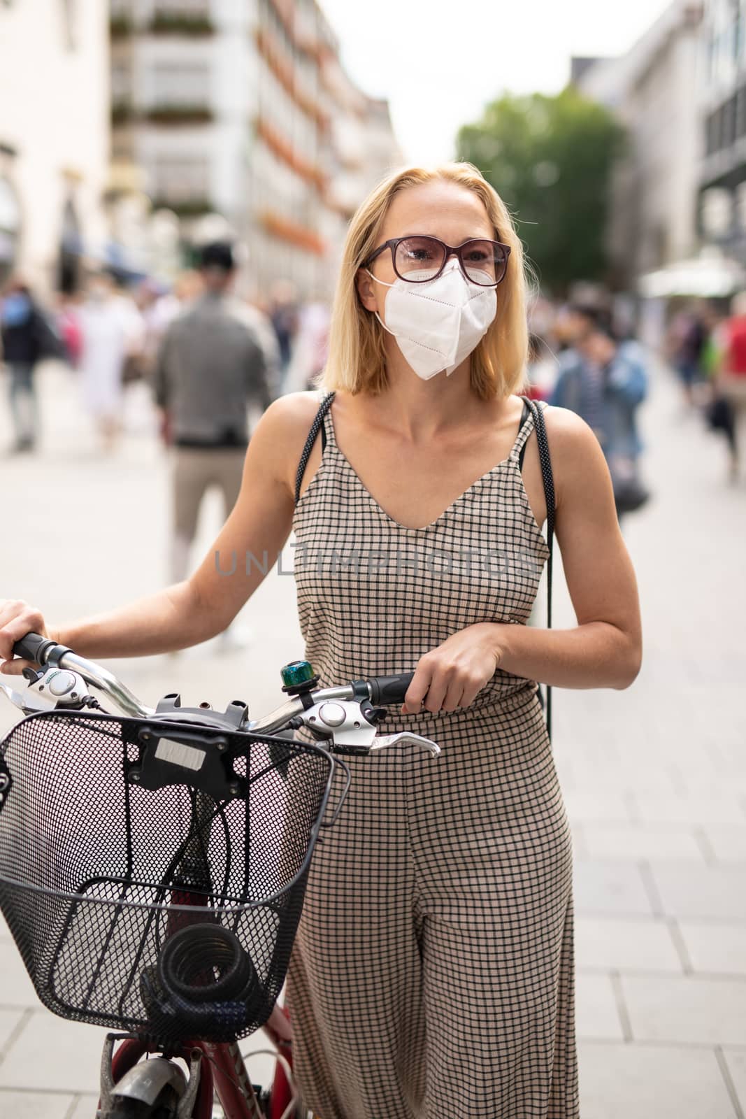 Woman walking by her bicycle on pedestrian city street wearing medical face mask in public to prevent spreading of corona virus. New normal during covid epidemic. by kasto