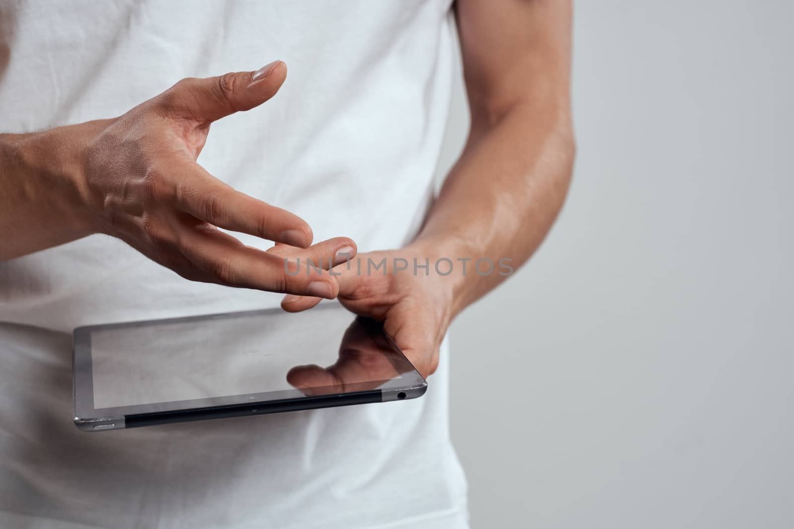 Tablet with a touch screen on a light background male hands white t-shirt cropped view. High quality photo
