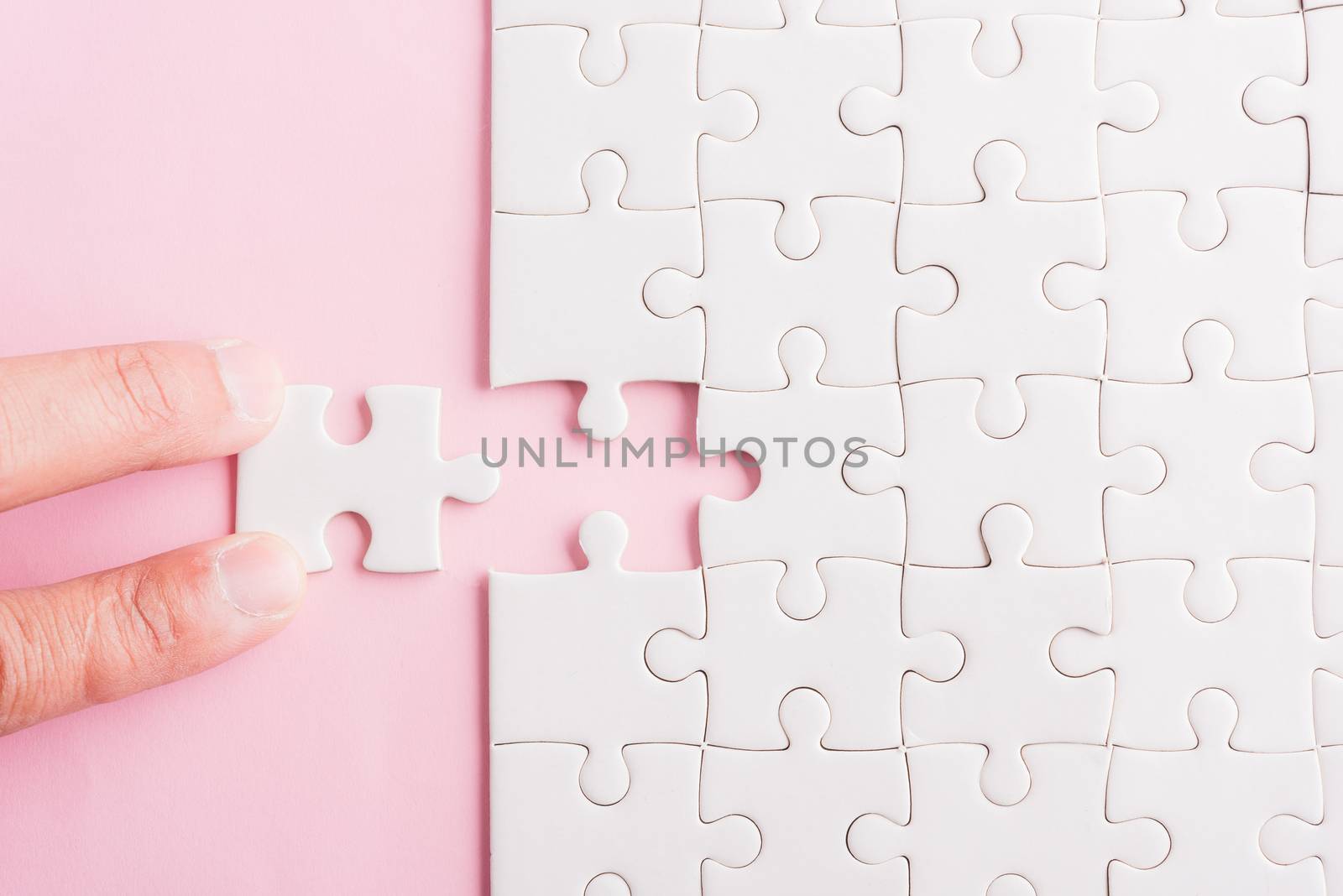 Top view flat lay of hand-holding last piece white paper jigsaw puzzle game last pieces put to place for solve problem complete mission, studio shot on a pink background, quiz calculation concept