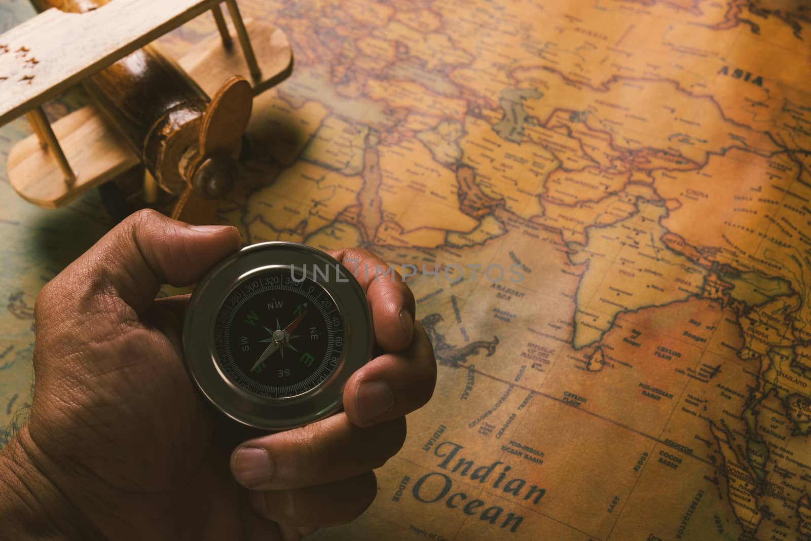 Hand hold old compass discovery and wooden plane on vintage paper antique world map background, Retro style cartography travel geography navigation