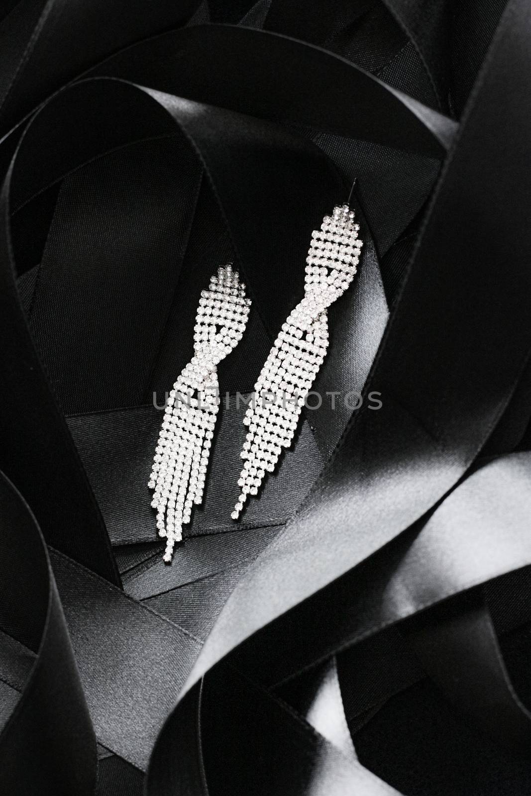 Luxury diamond earrings on black silk ribbon as background, jewelry and fashion brands