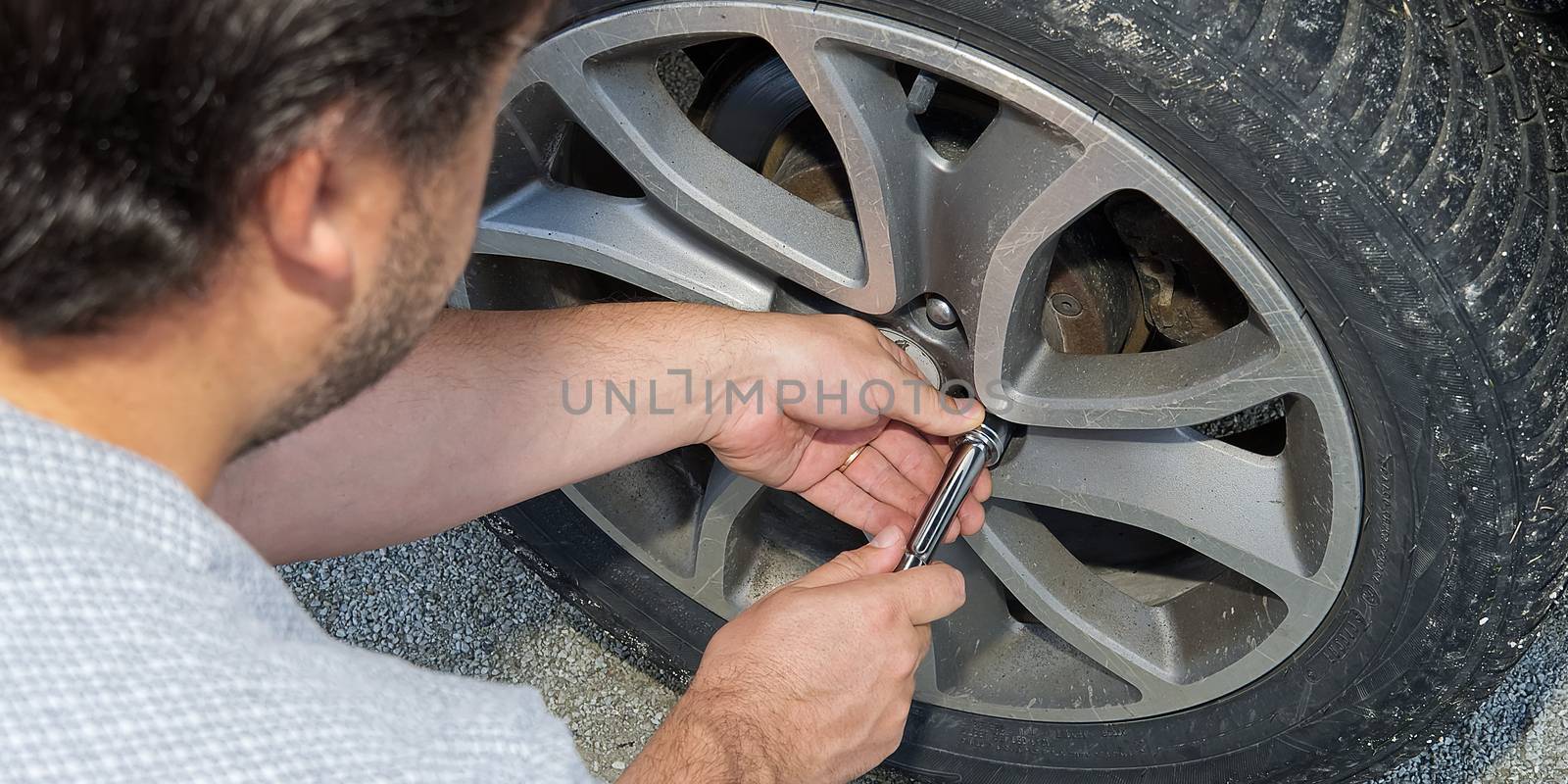 Man changing wheel. tire changer changing flat car tire. Help on road concept. Mechanic hands unscrews a flat tire of a car raised on a jack by PhotoTime