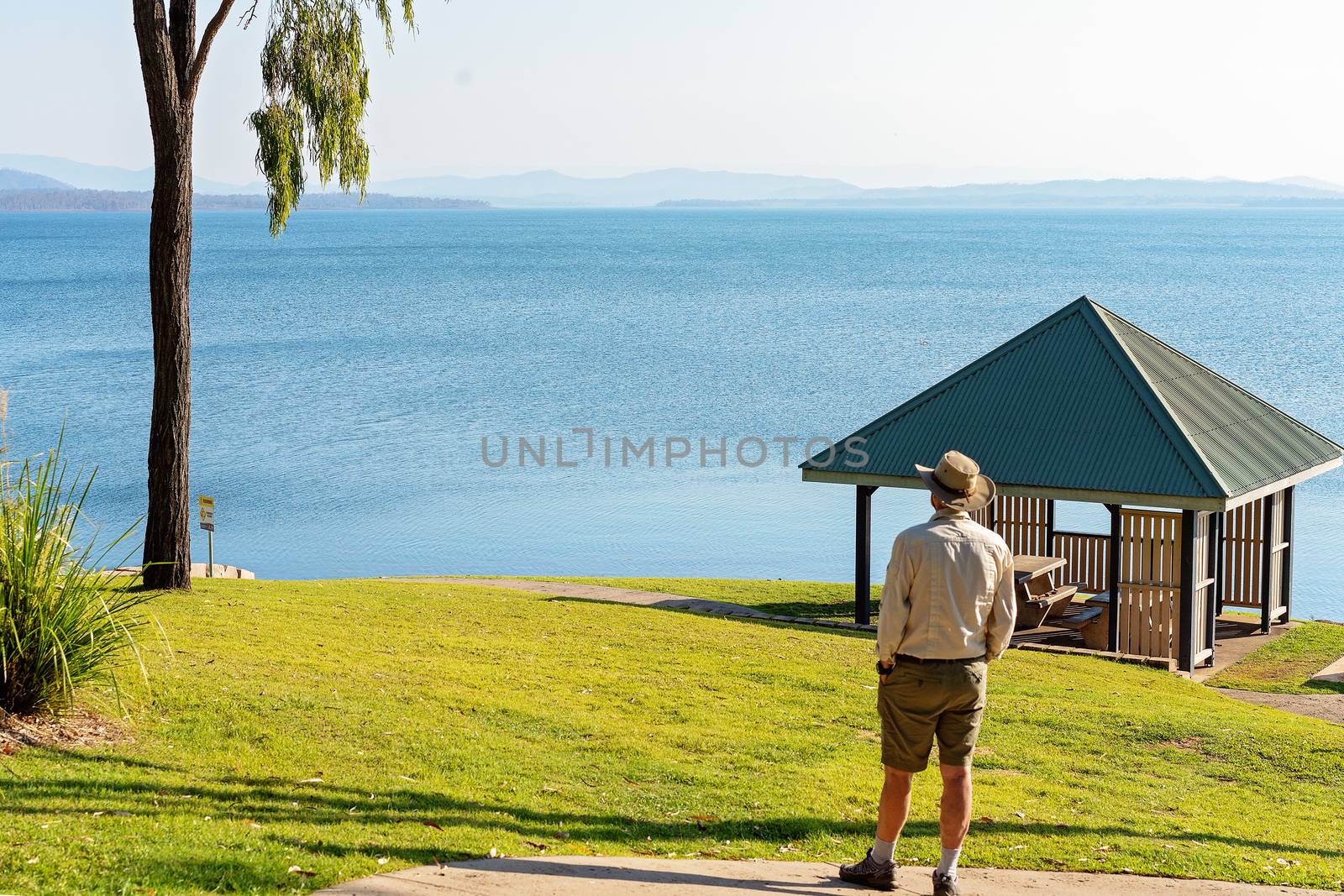 Senior male retiree standing looking out over a large dam popular for public recreation