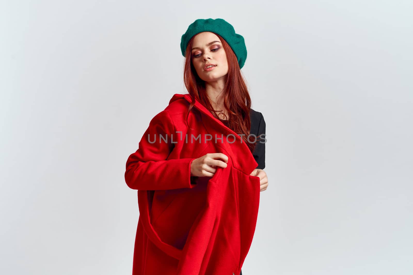 A woman holds in her hand a red coat and a dark T-shirt Green hat cropped view of a light background. High quality photo