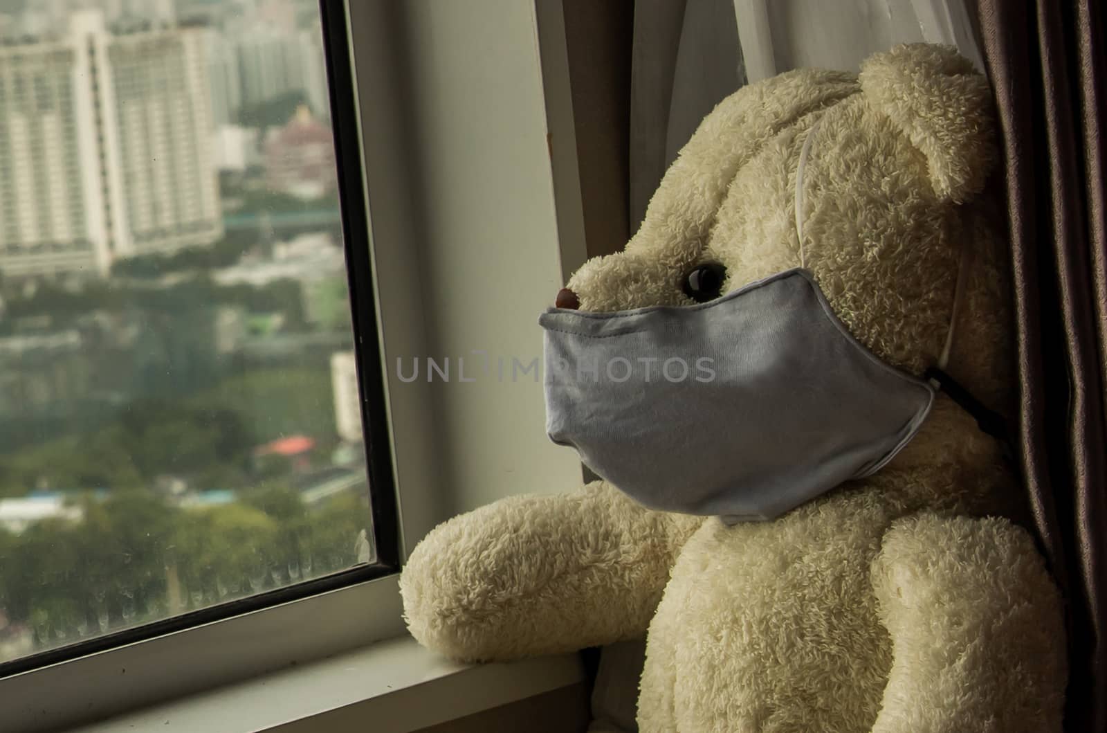 Close-up of Sad teddy bear in protective medical masks sits on windowsill and looks out window. Stay at home quarantine coronavirus pandemic prevention, Virus outbreak in a world. No focus, specifically.