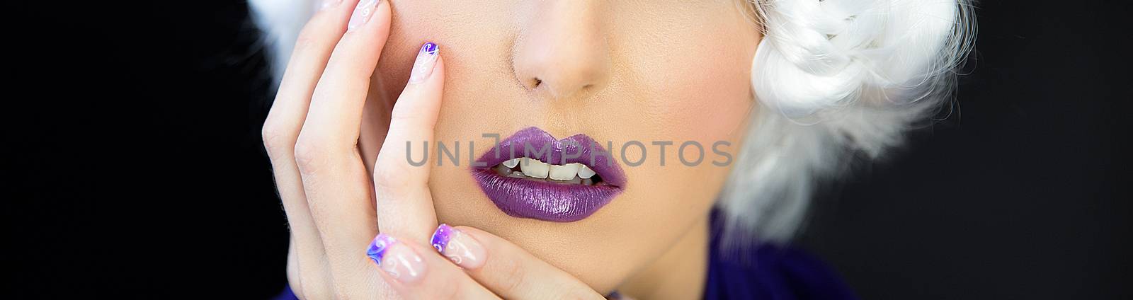 Close up of the lower face of a beautiful young woman wearing purple lipstick and nail polish