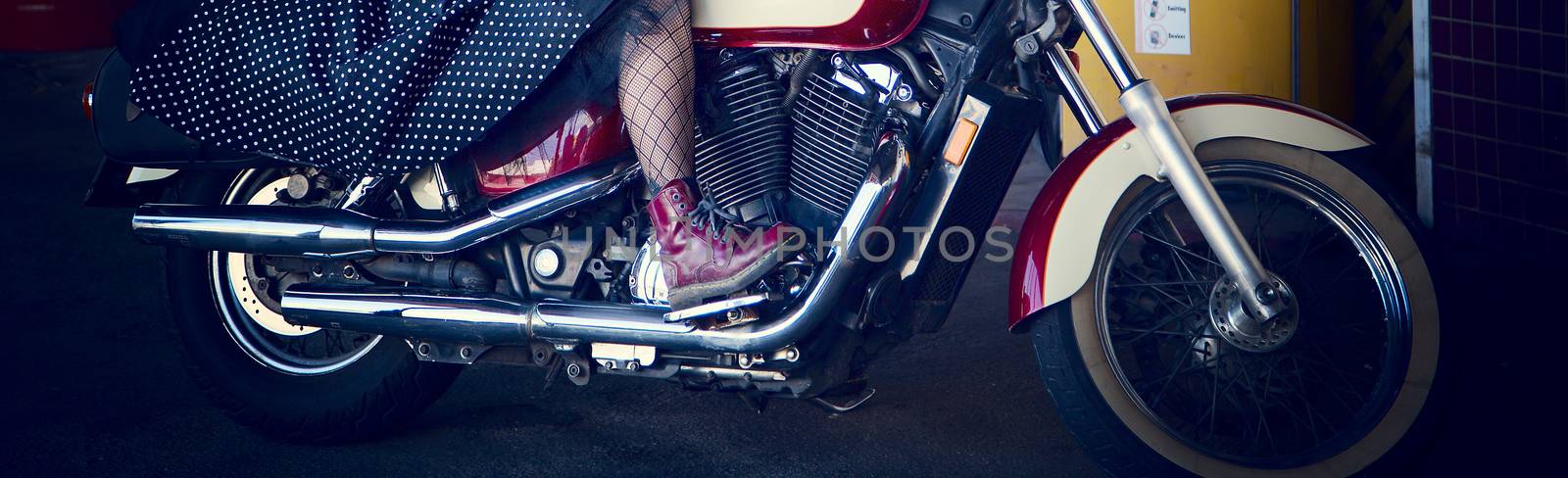 Close up of a woman's leg encased in net stockings and wearing a red boot, riding a motorcycle