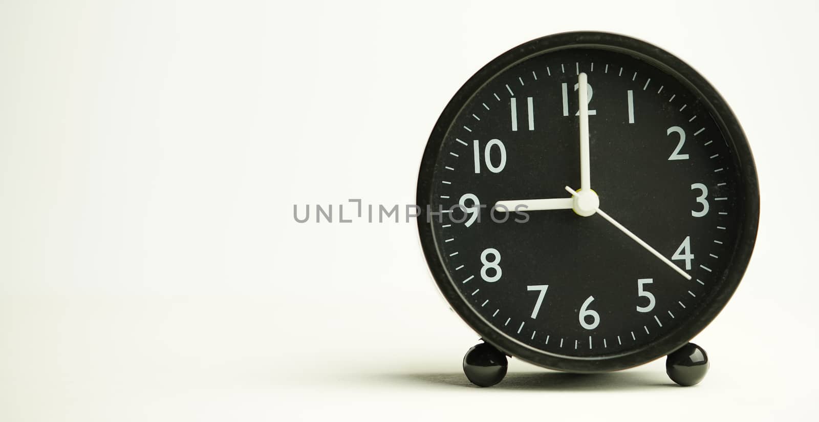 Decorative close-up black alarm clock at 9 o'clock isolated on white background with abstract copy space, start time of working day.
