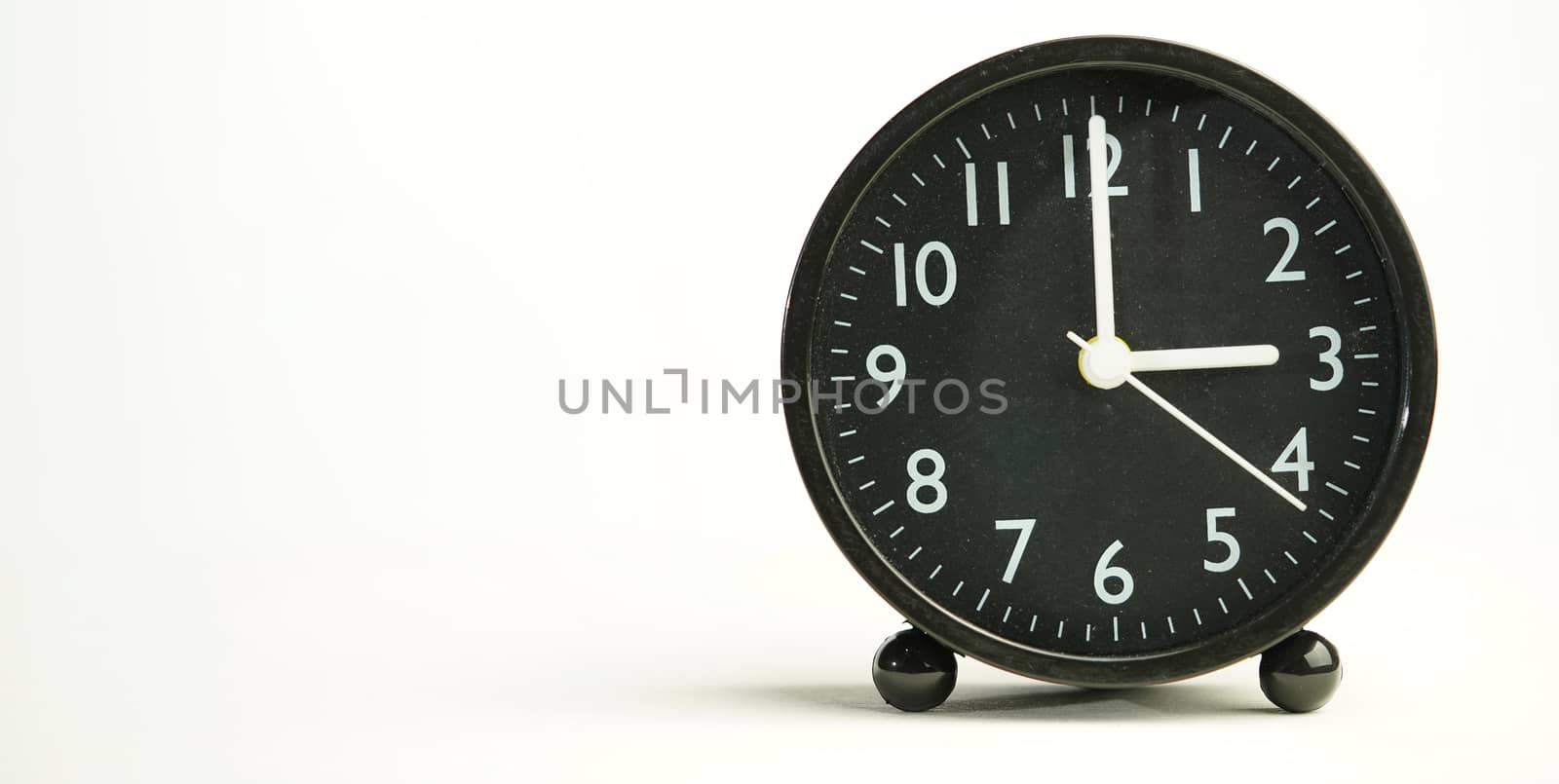 Decorative close-up black analog alarm clock for 3 o'clock or 15 o'clock, separate white background with copy space.