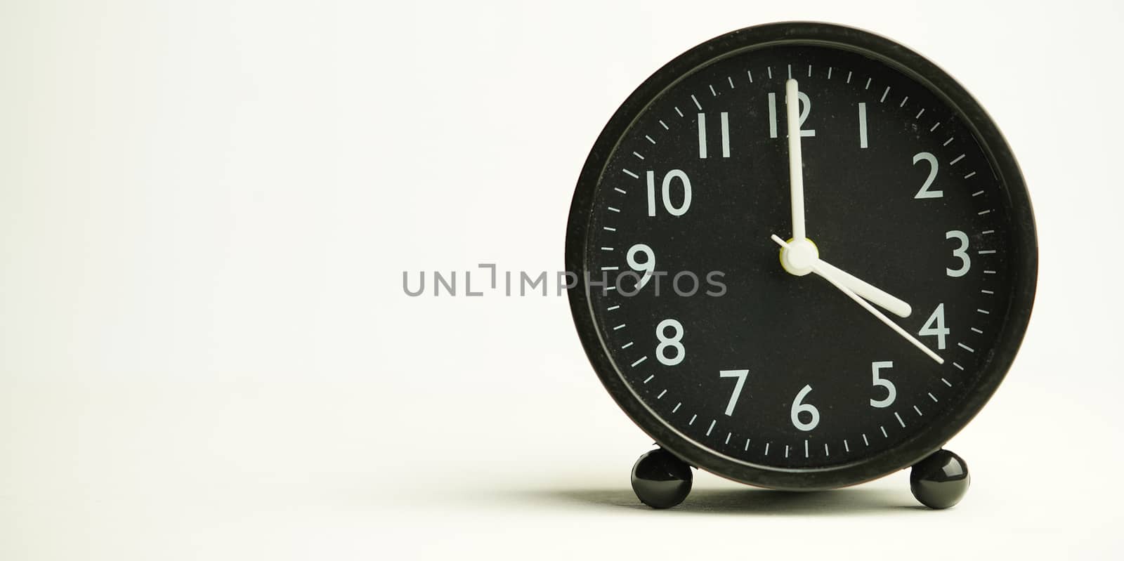 Decorative close-up black analog alarm clock for 4 or 16 o'clock, separate white background with copy space.