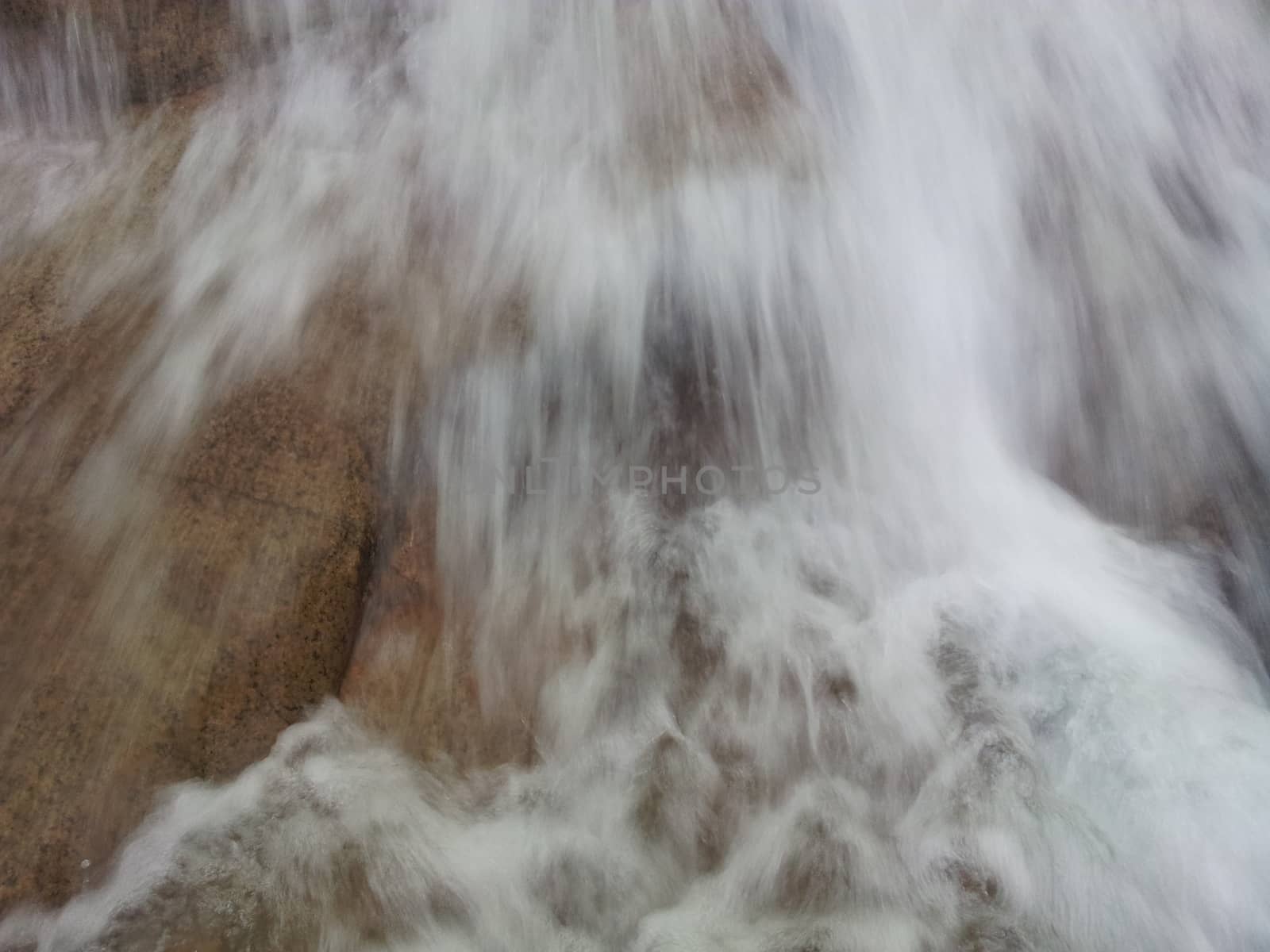 Blurred or unfocused view of flowing water stream in between stones by Photochowk