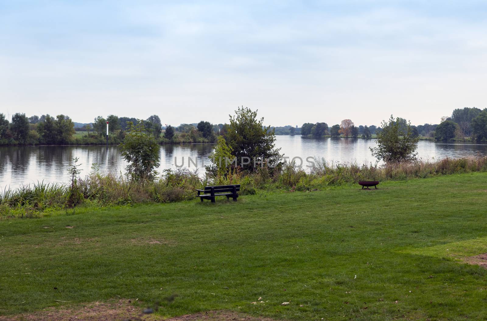 the river maas in holland with bench and fireplace at the border of the water, the maas is a river for watersport but also for water transport