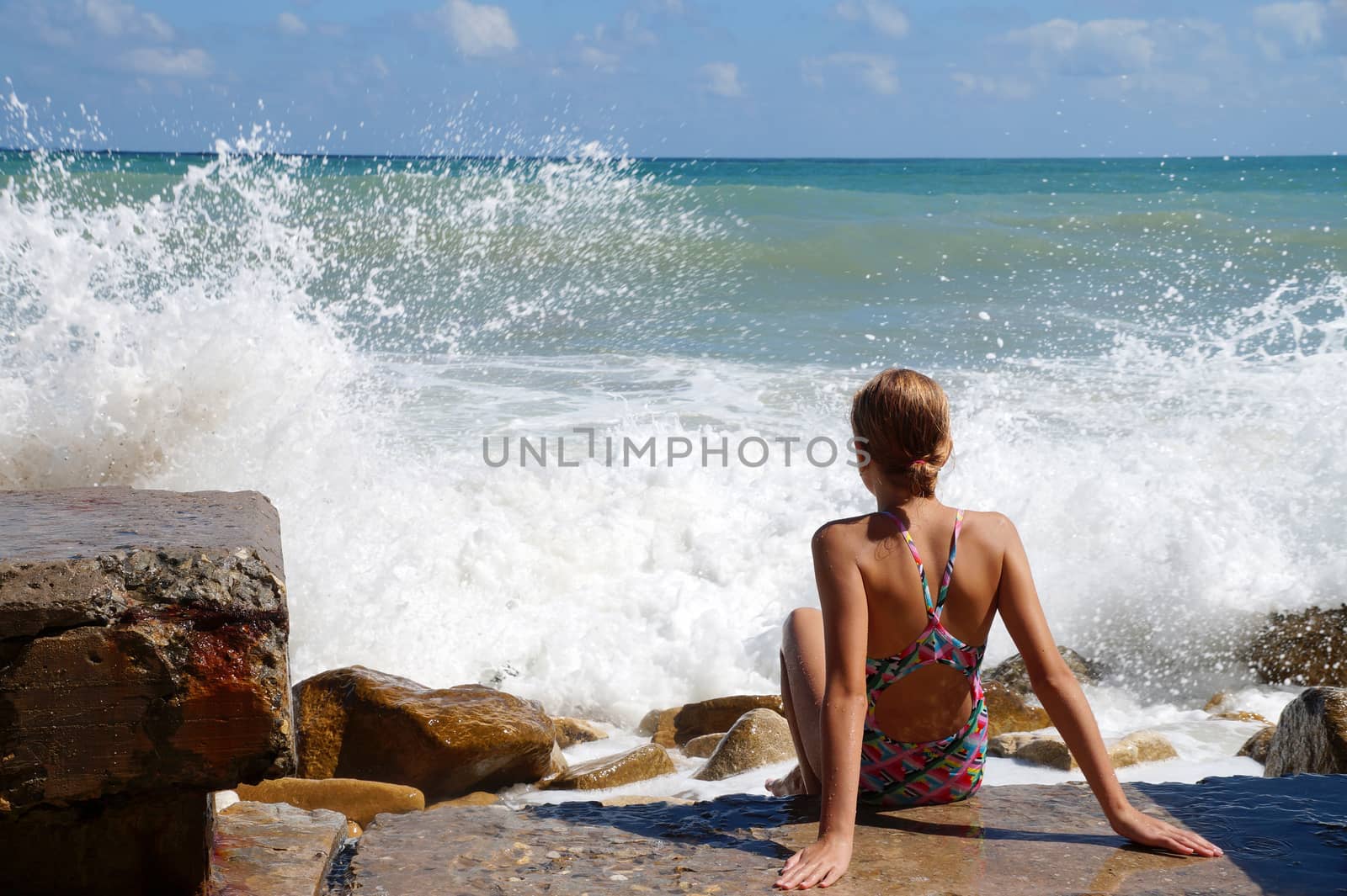 teenage girl sitting on a sandy beach in sea white foam.