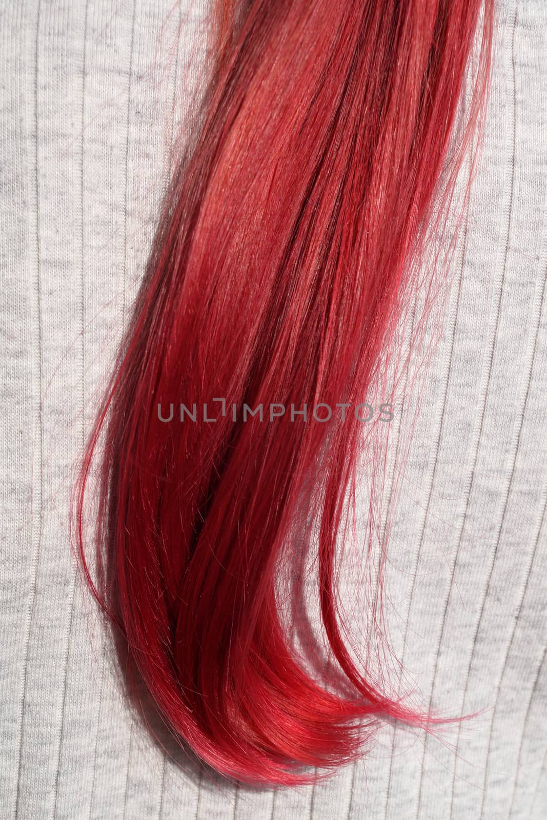 strand of dyed red female hair on a light background close-up