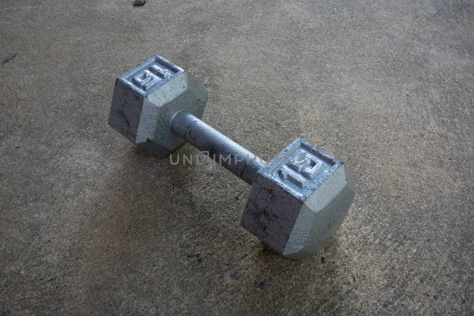 A Silver Fifteen Pound Dumbbell on Concrete by bju12290