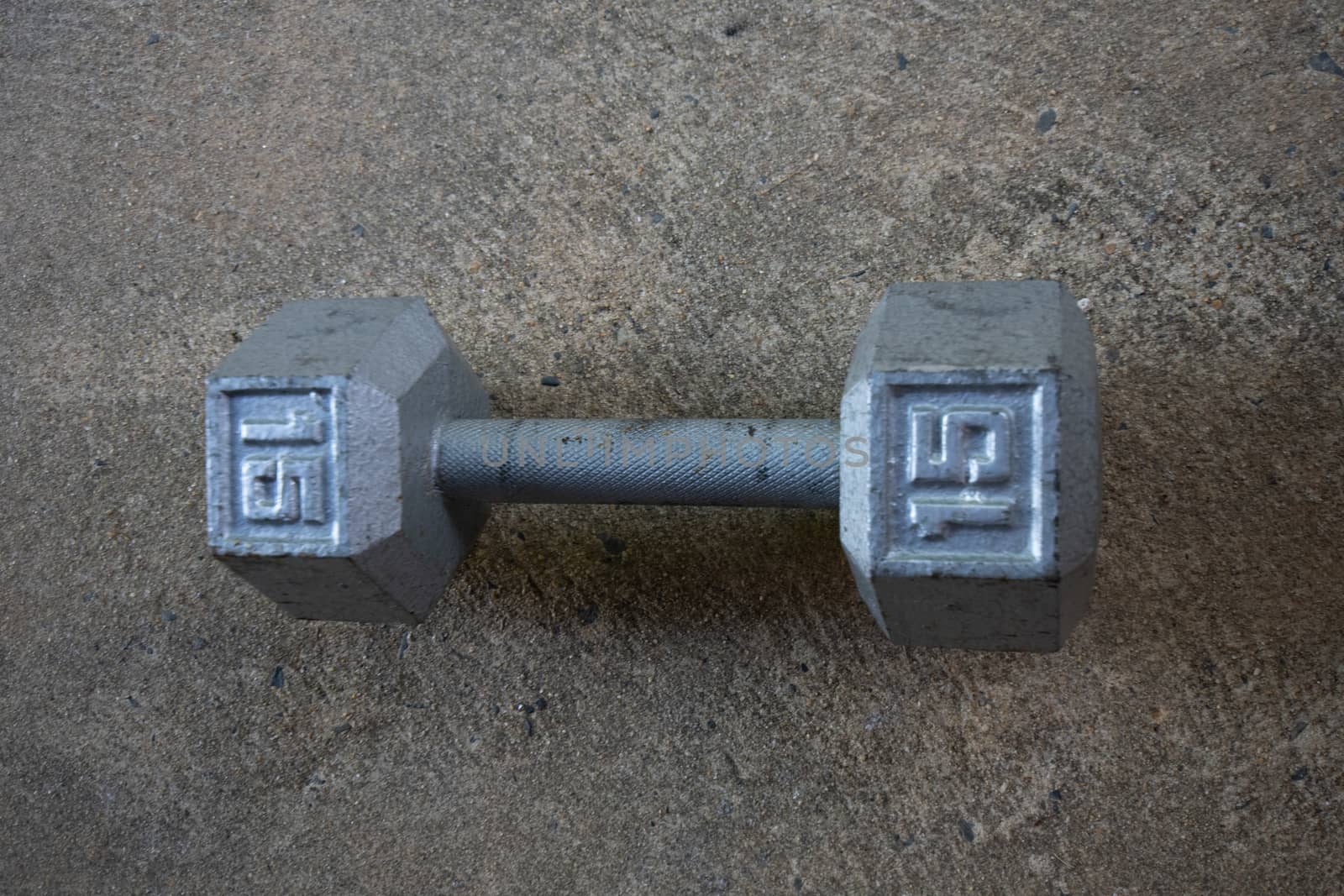 A Silver Fifteen Pound Dumbbell on Concrete by bju12290