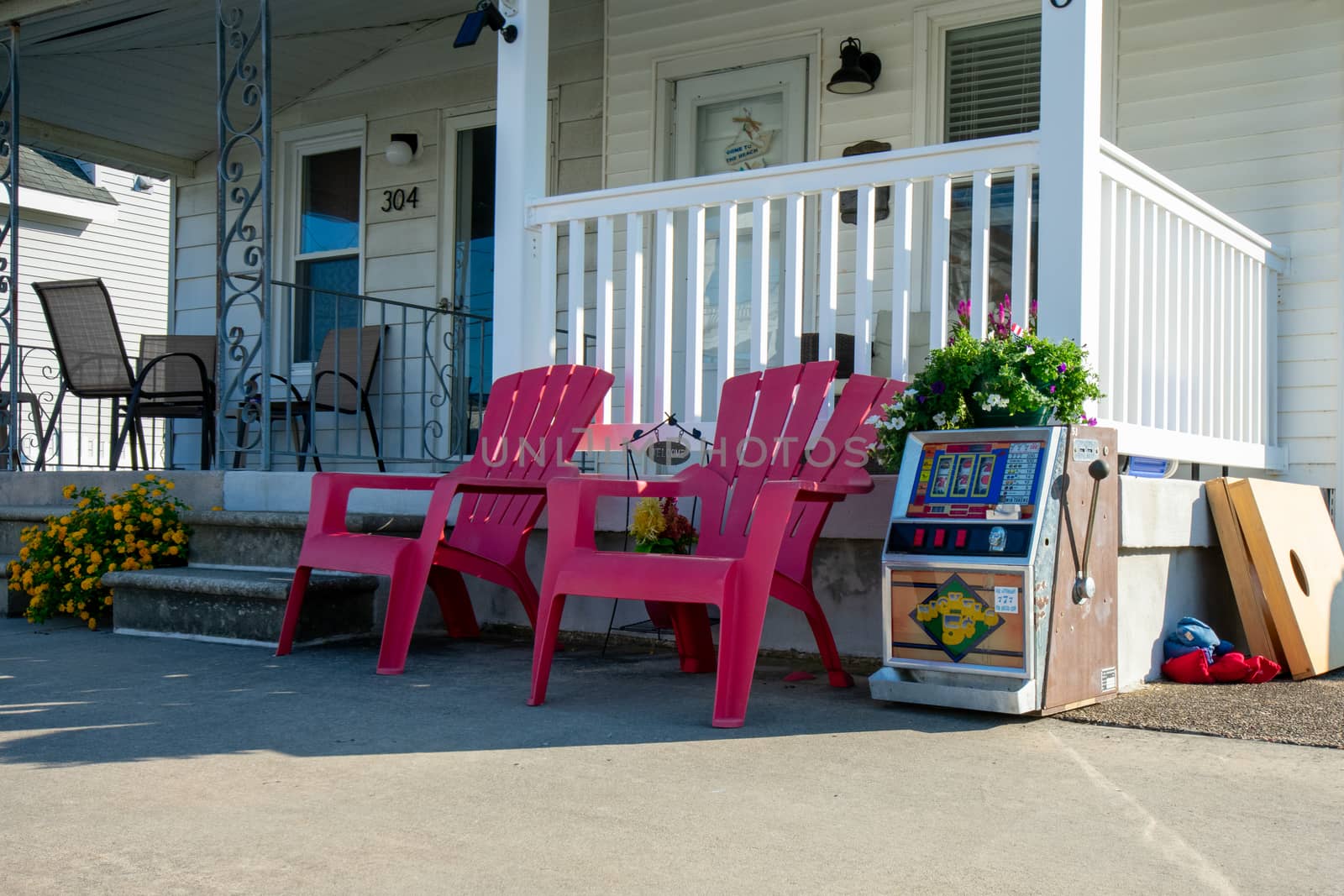 The Front of a Beach House With Two Red Lawn Chairs and a Slot Machine Next to Them