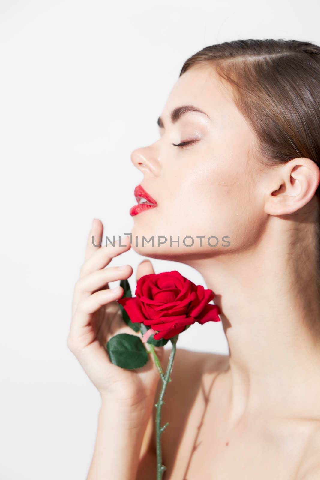 Woman with rose sniffs a flower with her eyes closed bright makeup light background