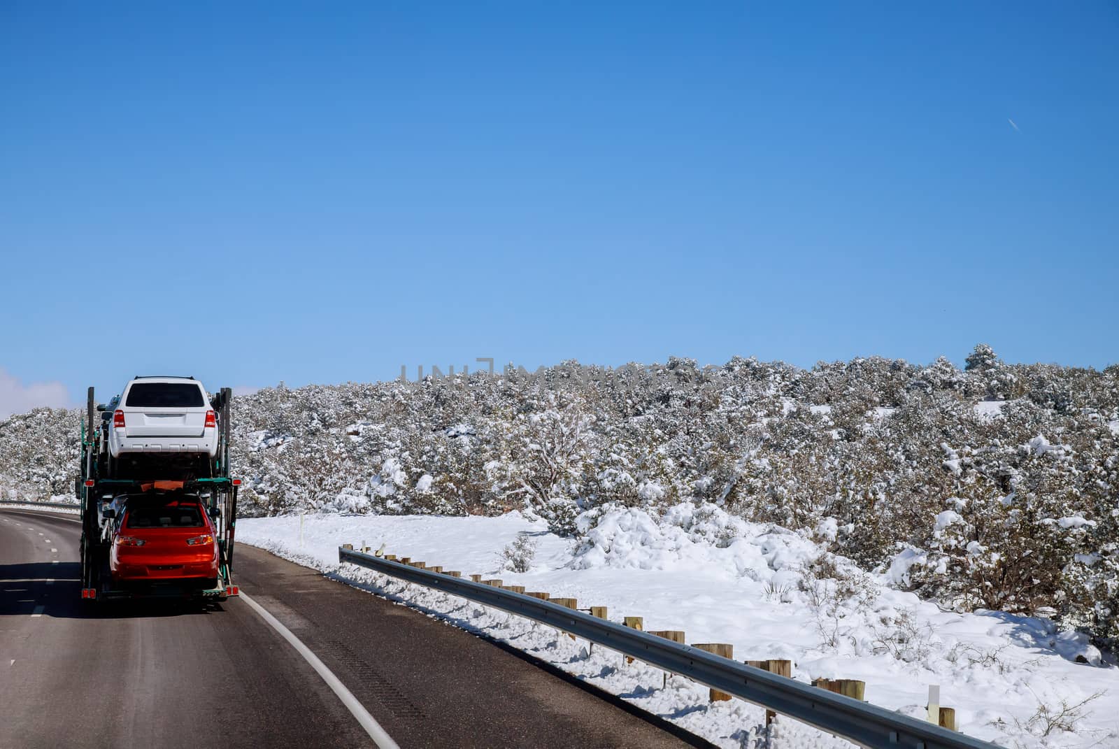 The trailer transports cars on highway winter road with snow landscape in the mountains