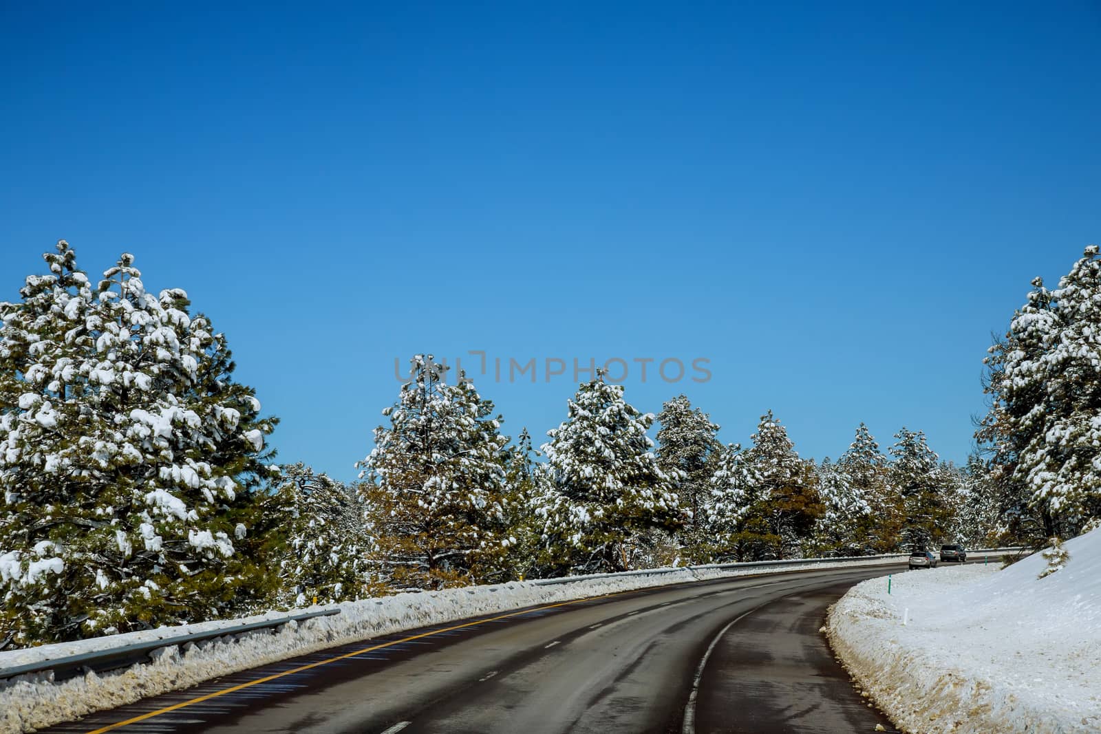 View of a curving road covered in snow way road during winter time, snow mountains in the distance. by ungvar