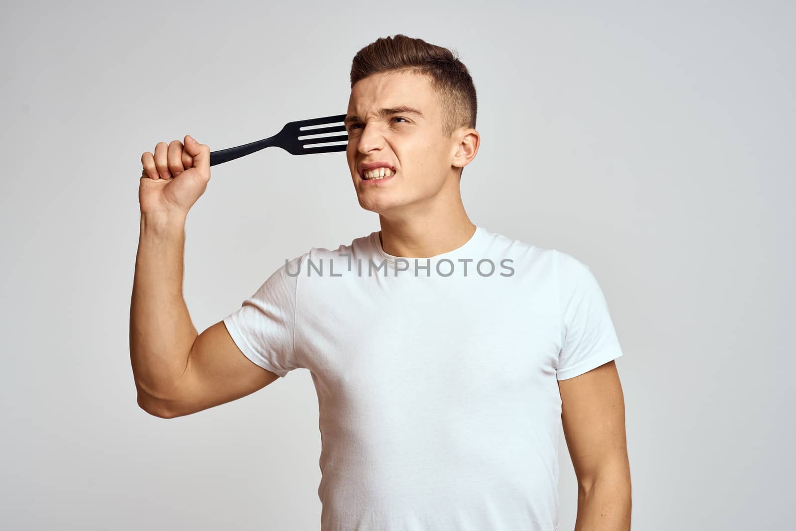 Guy with kitchen tools in hands on a light background cropped view of emotions fun model. High quality photo