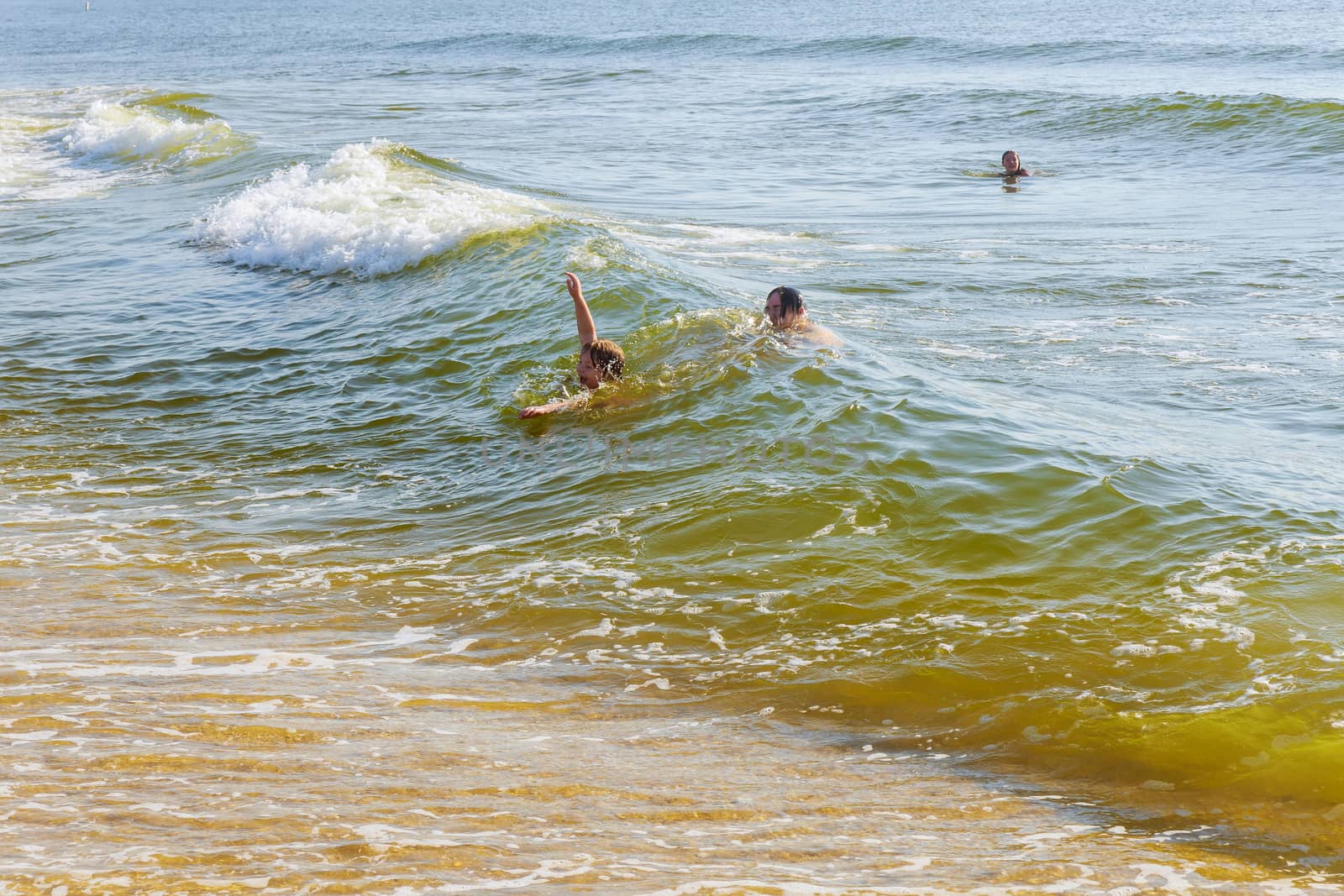 Girl an dboy swimming in the big wave of the ocean.