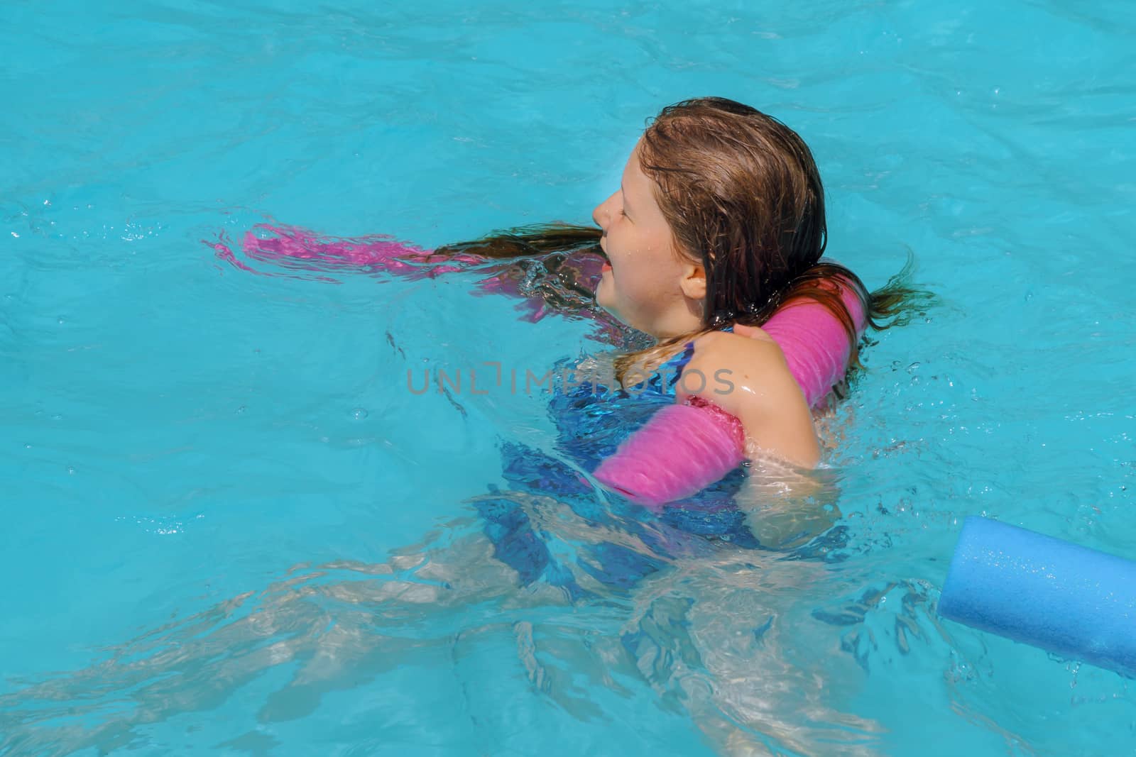 Young girl swimming with float sticks in blue water.