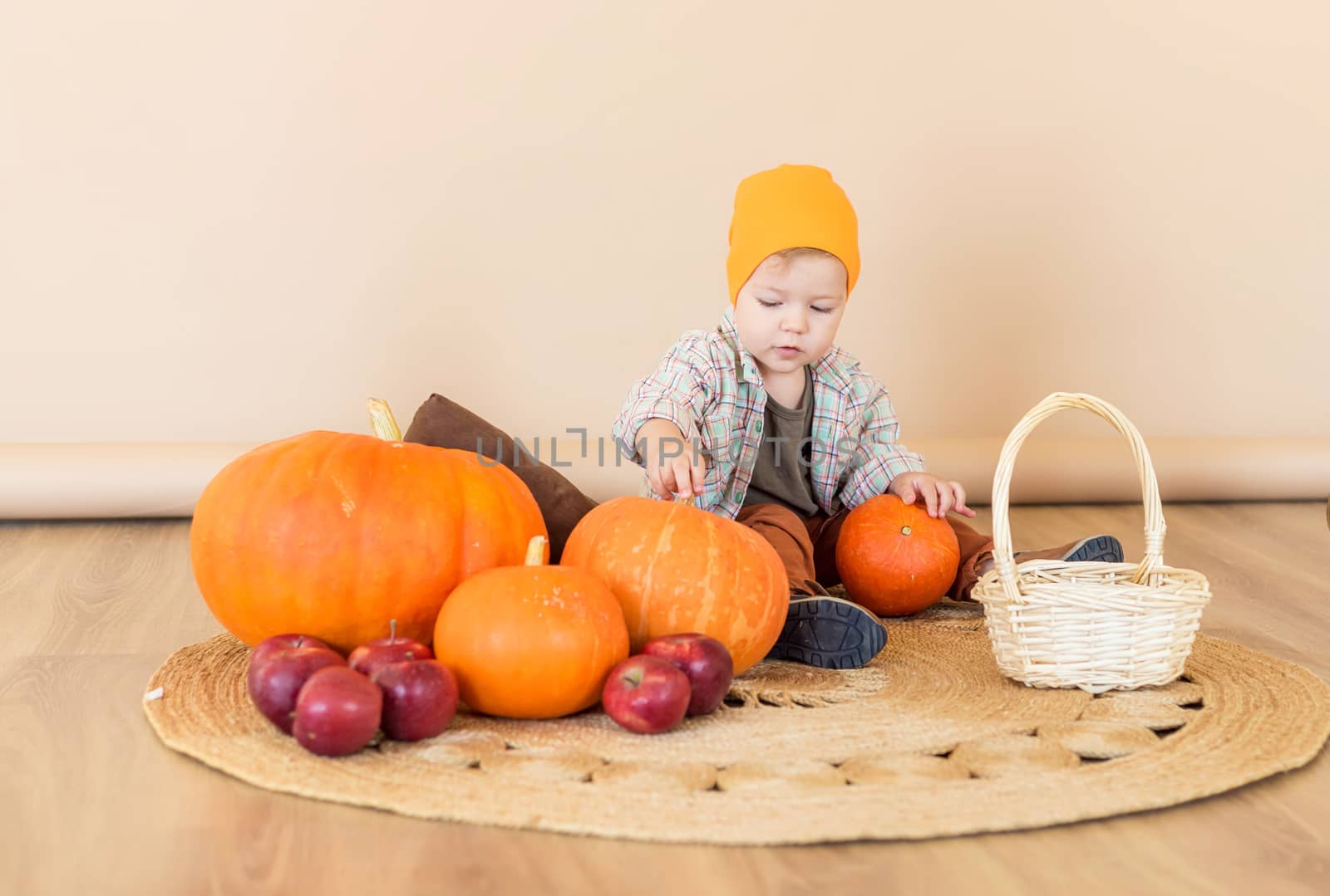 A little kid sits among pumpkins in an autumn photo zone in the studio to celebrate thanksgiving day. Celebrations concept