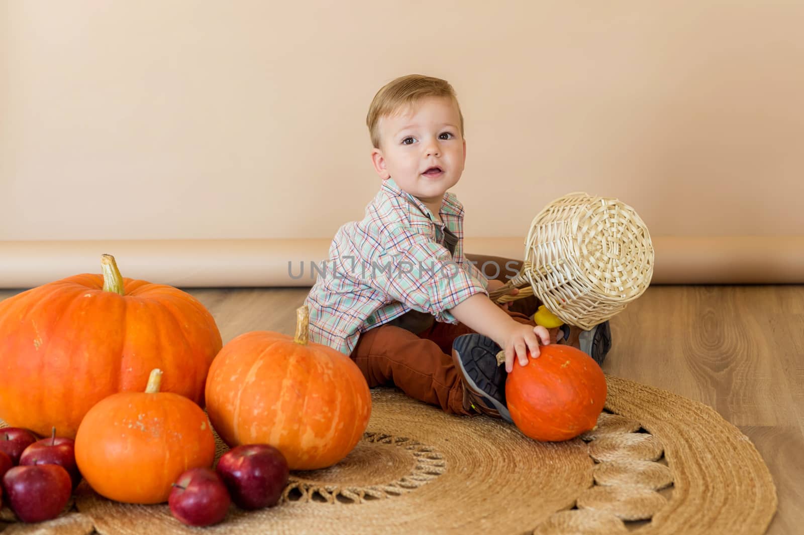 A little kid sits among pumpkins in an autumn photo zone in the studio to celebrate thanksgiving day. Celebrations concept