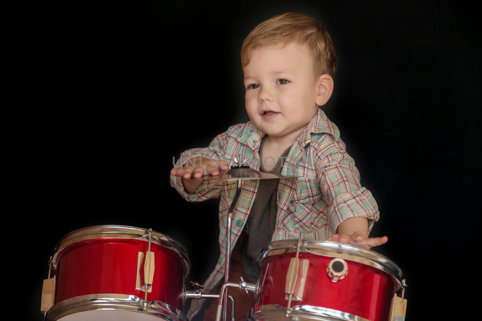 Two year caucasian boy is Playing Drum Set Isolated on Black Background.
