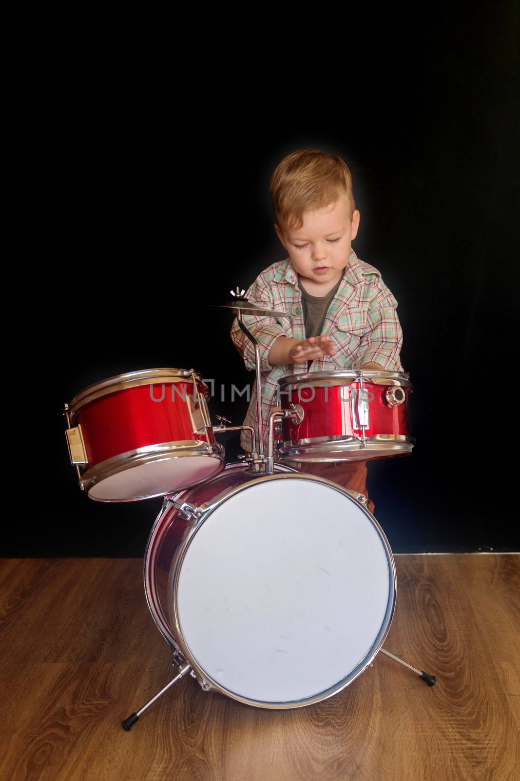 Two year caucasian boy is Playing Drum Set Isolated on Black Background.