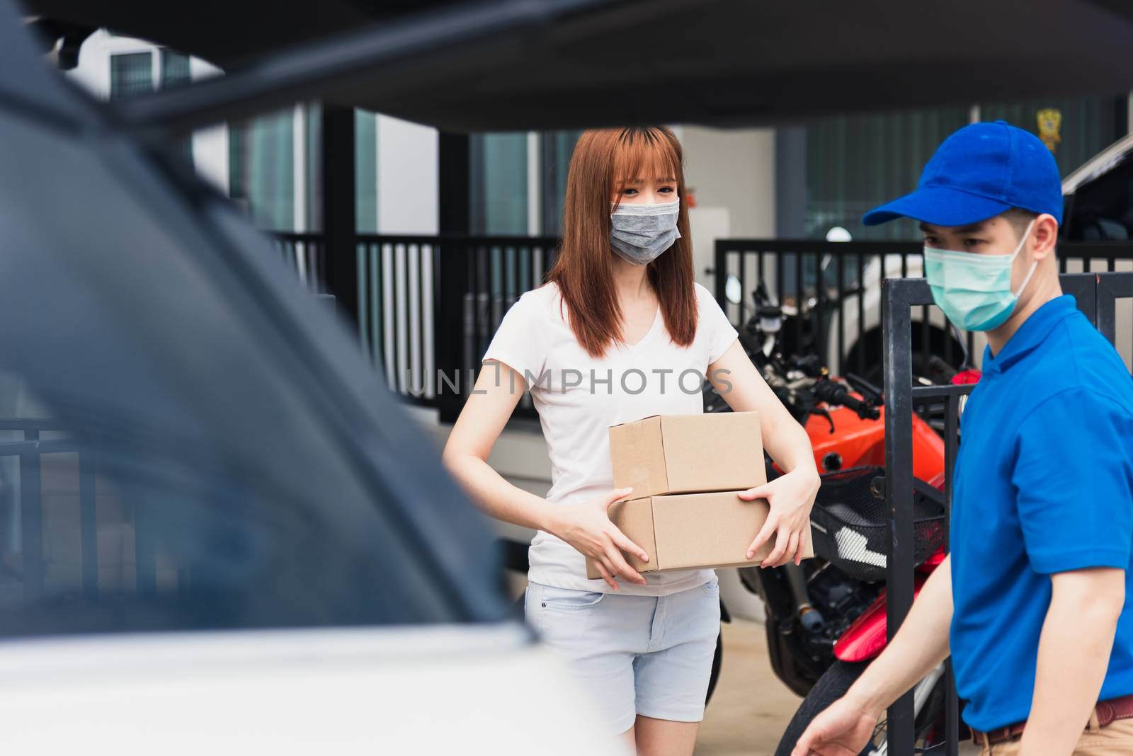 Asian young delivery man courier shopping online give package post box he protective face mask service woman customer receiving box at front home, under curfew quarantine pandemic coronavirus COVID-19