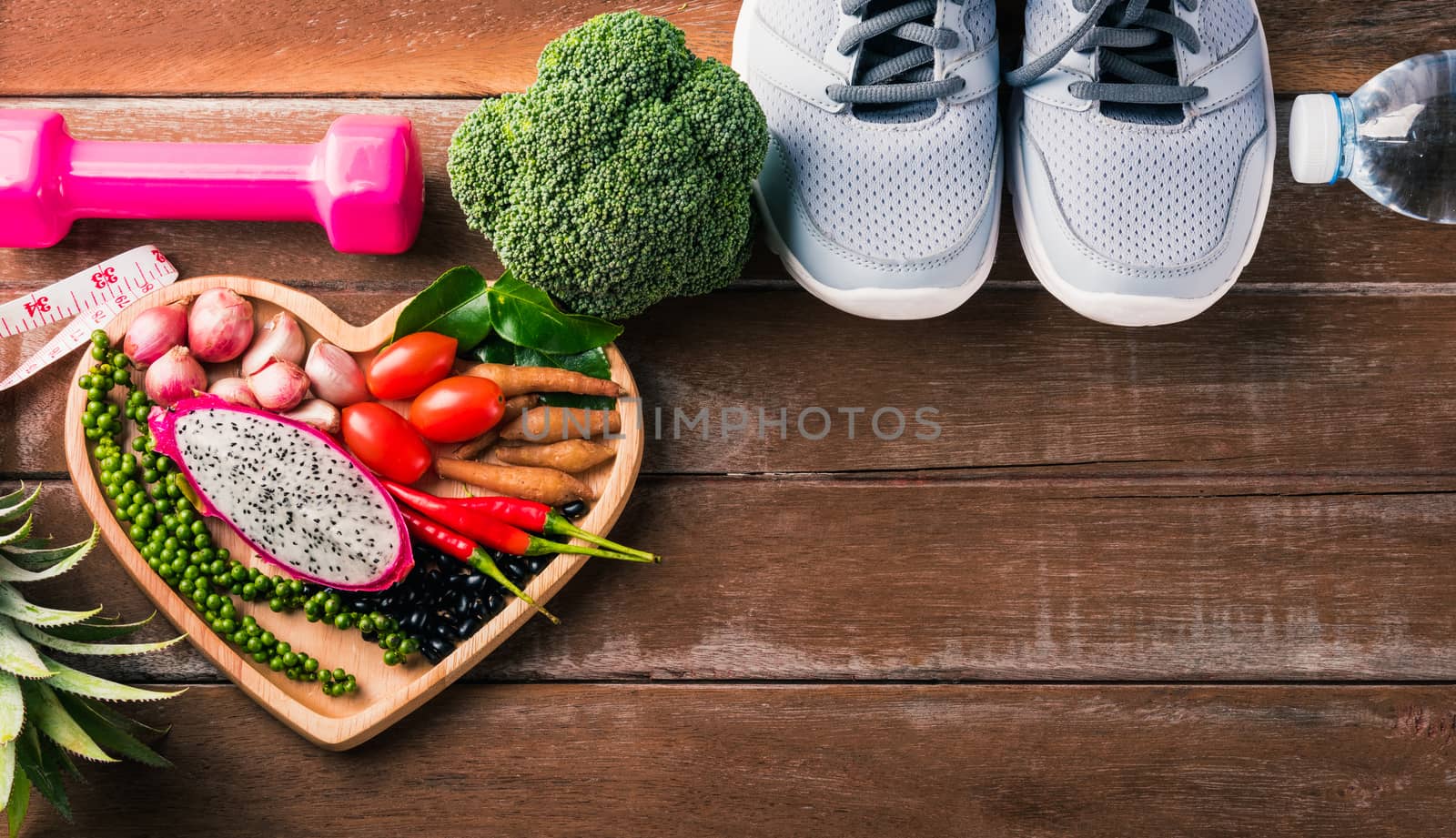 Top view of various fresh organic fruit and vegetable in heart plate and sports shoes, dumbbell and water, studio shot on wooden gym table, Healthy diet vegetarian food concept, World food day