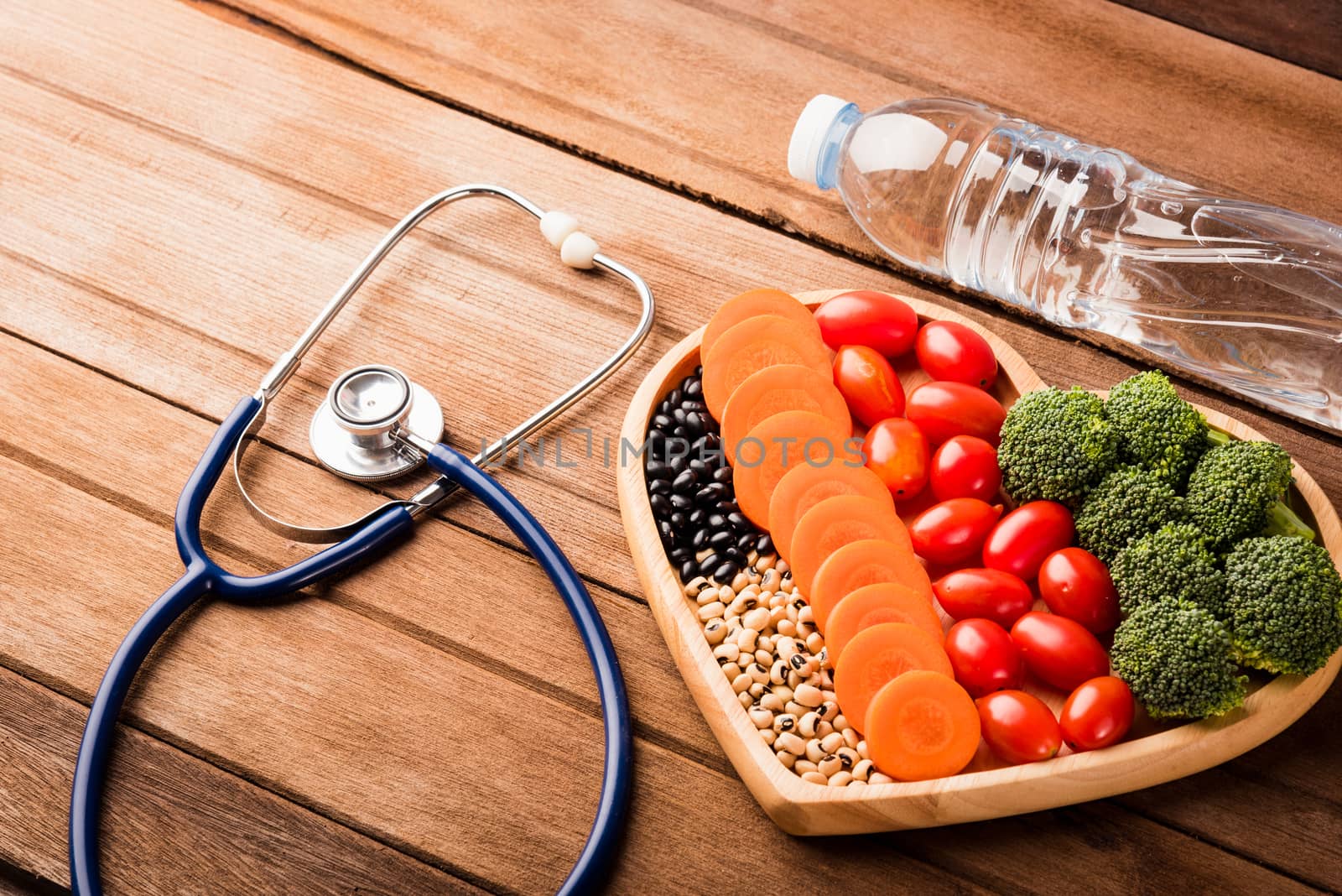 Top view of fresh organic fruits and vegetables in heart plate wood (carrot, Broccoli, tomato), doctor stethoscope and plastic water bottles on wooden table, Healthy lifestyle diet food concept
