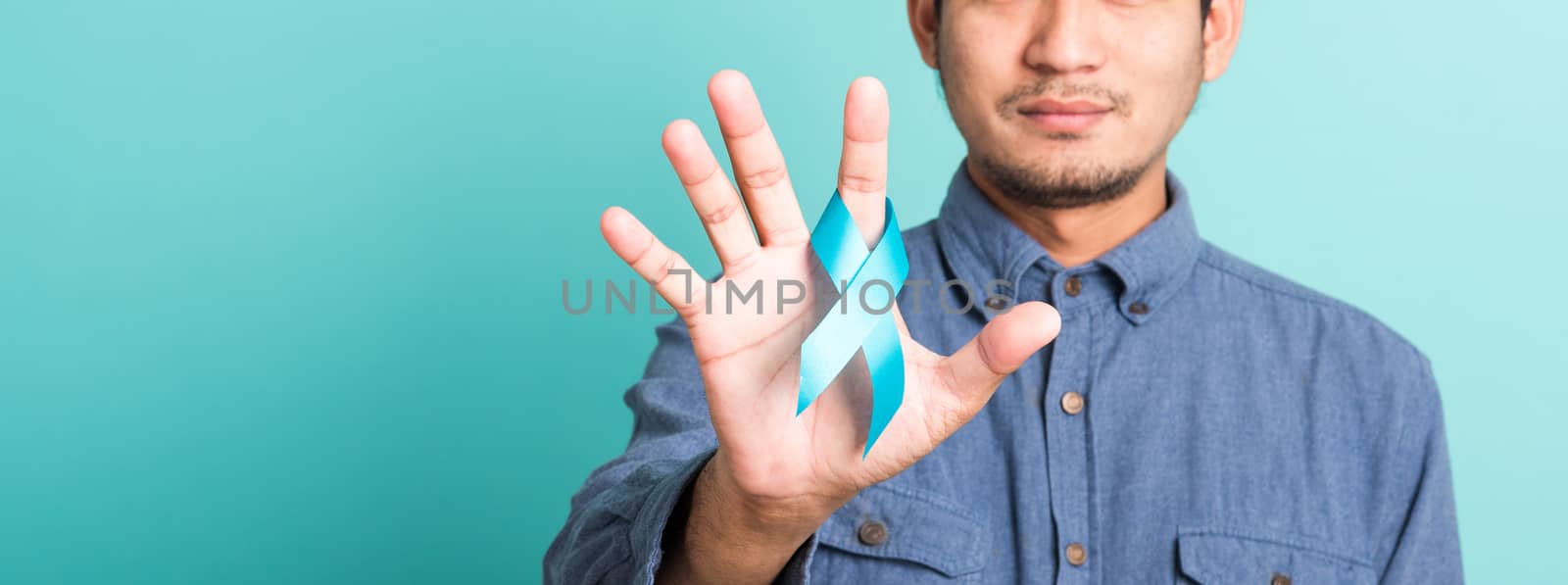 Asian portrait happy handsome man posing he holding light blue ribbon for supporting people living and illness, studio shot isolated on blue background, Prostate Cancer Awareness in November concept