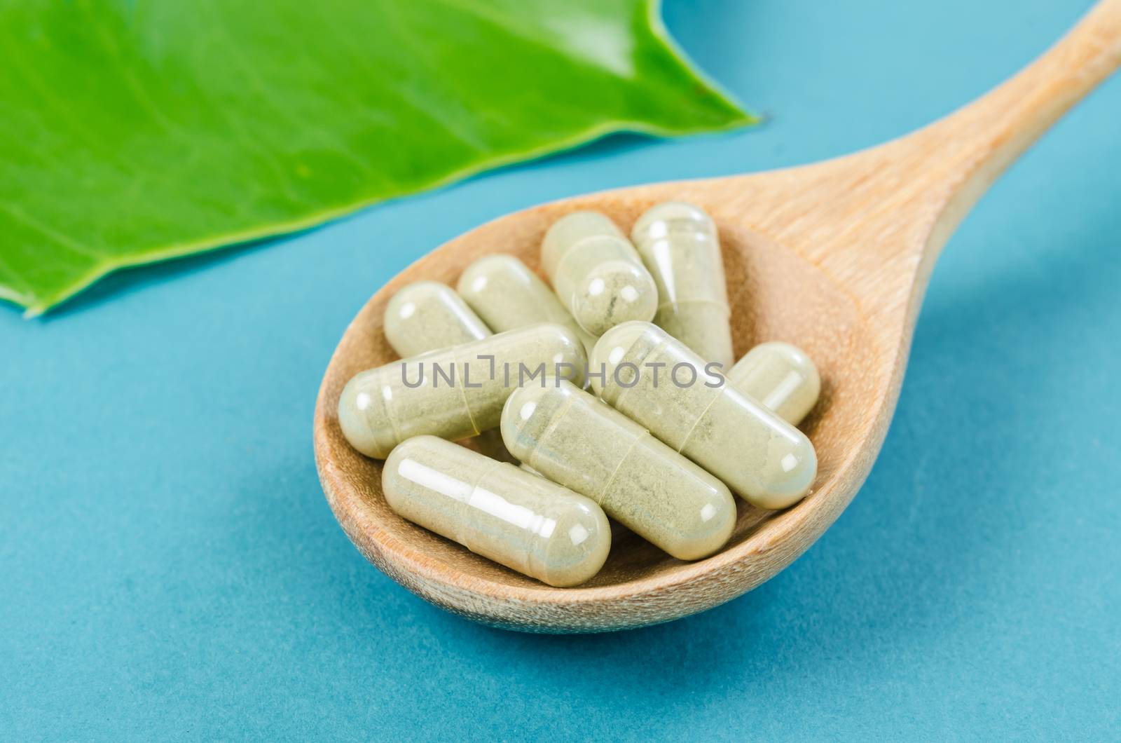 Herbal capsules from herbs in wooden spoon with green leaf for healthy. Lifestyle concept.