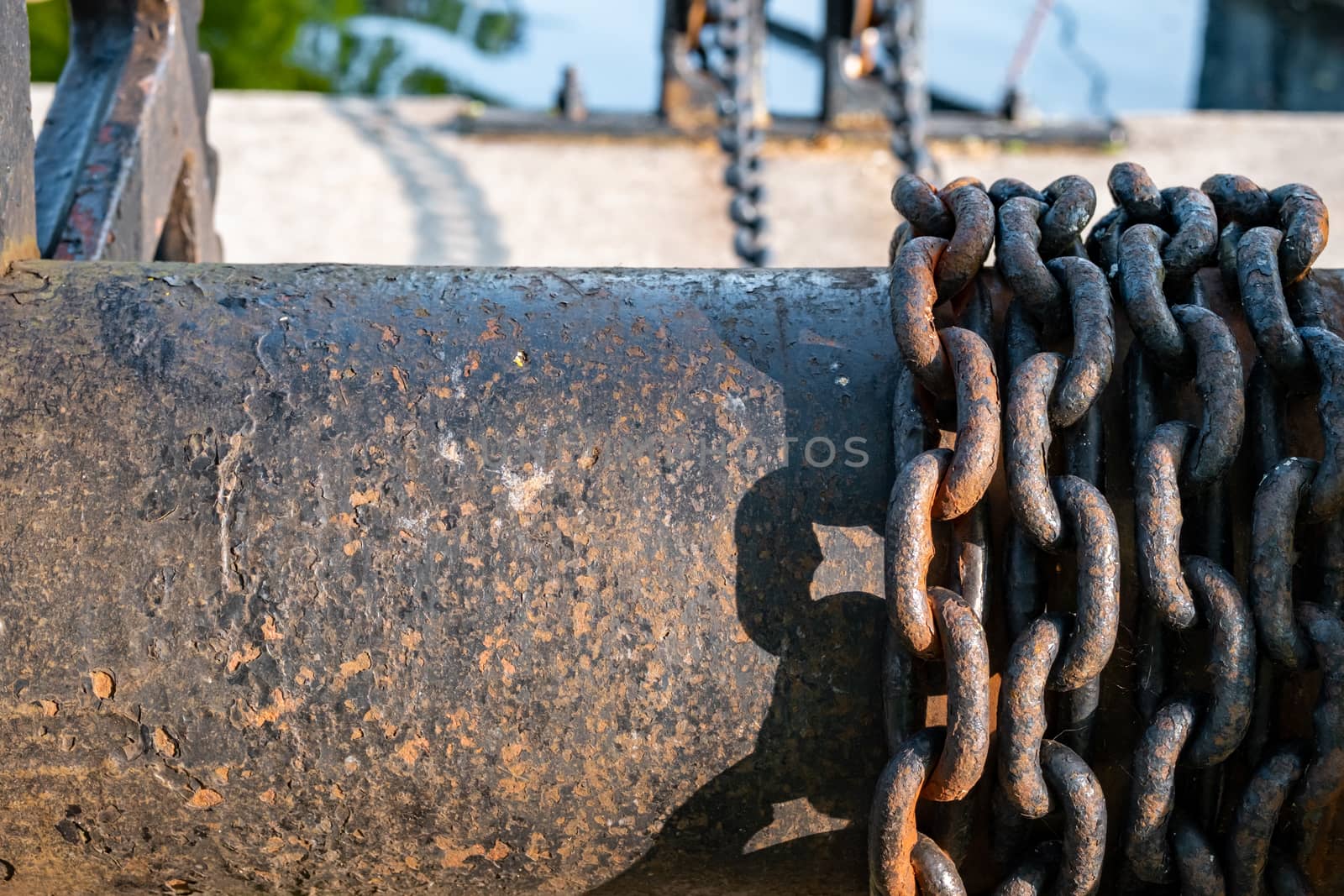 Rusting iron chains are wrapped around a large metal spool, visibly continuing suspended in the background.