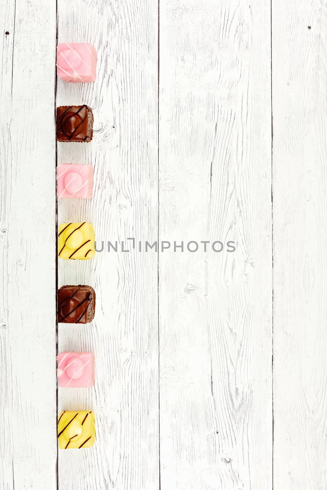 Row of miniature colorful iced cakes on board background with space for copy text, top view flat lay