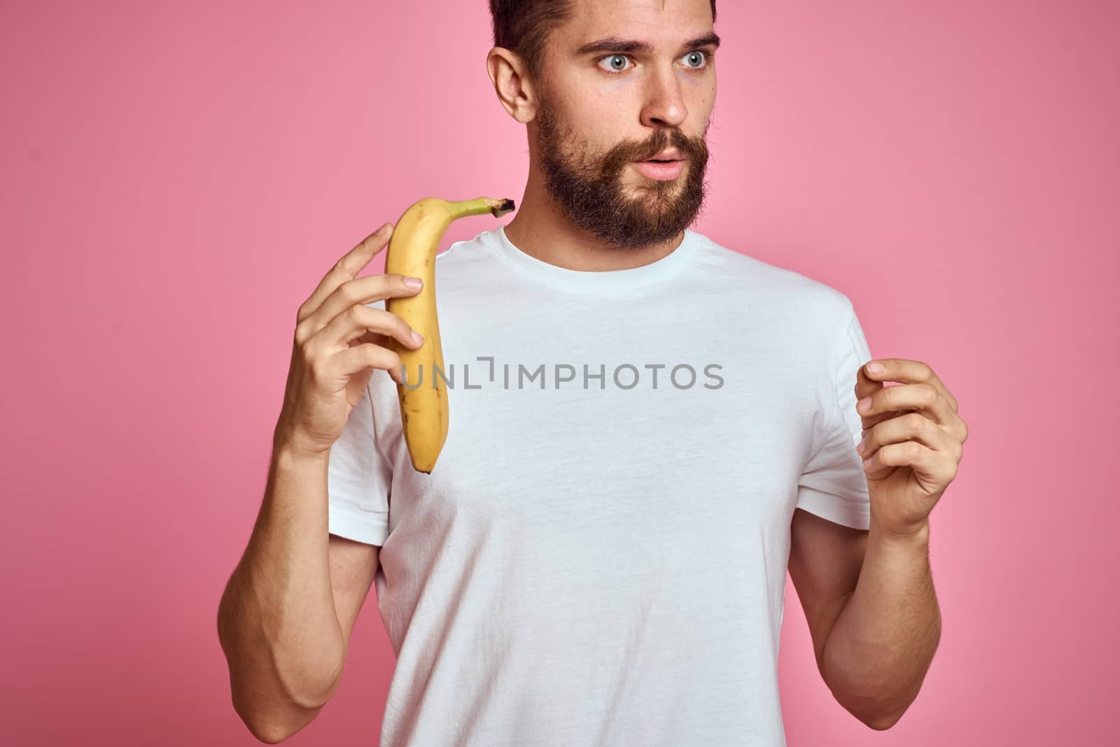 bearded man with banana in hand on pink background fun emotions model. High quality photo