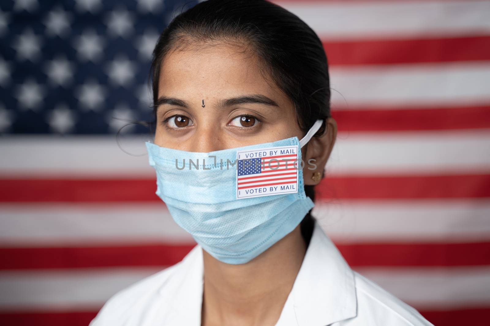 Close up face of Girl with I voted by main sticker on her medical mask with US flag as background - Concept of mail in voting in US election