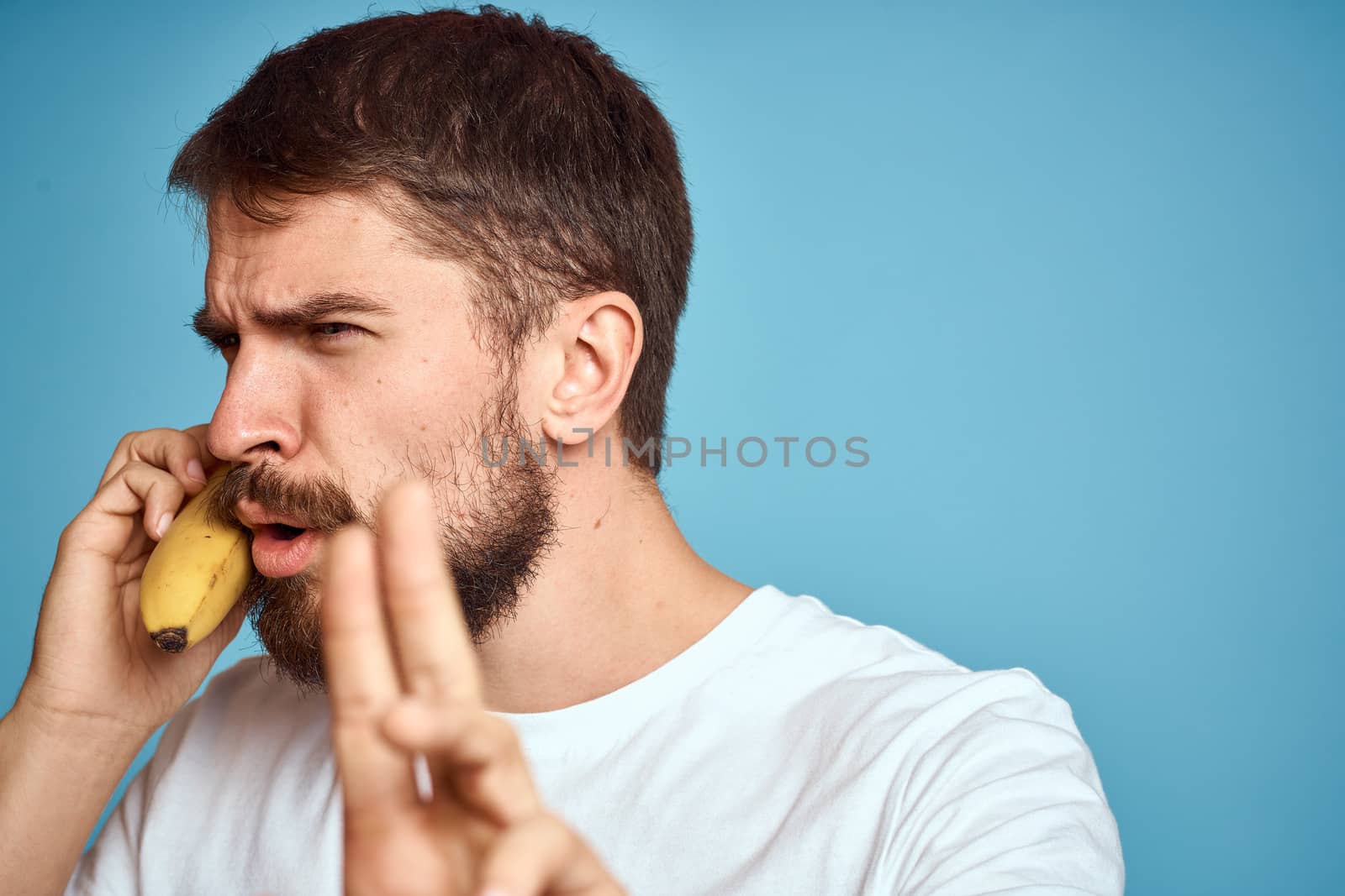 a man with a banana is caught in a white t-shirt on a blue background concept of communication by phone. High quality photo
